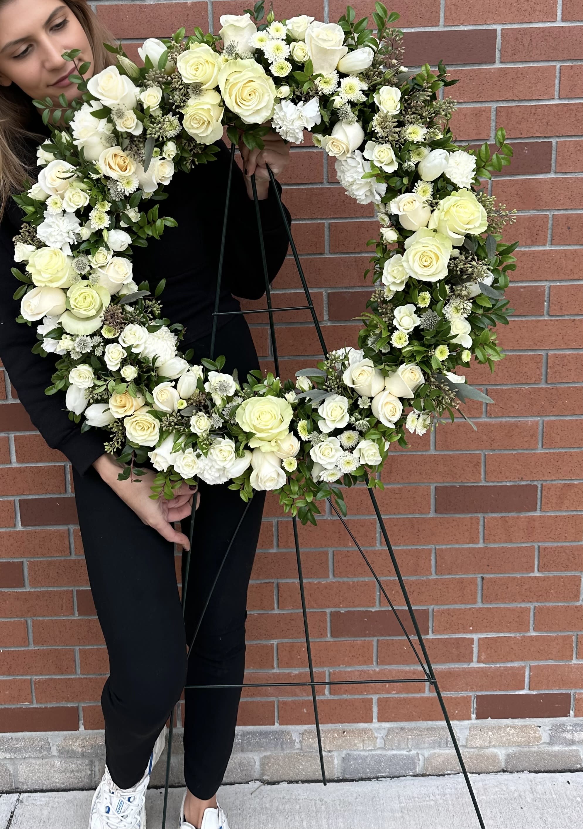 White Sympathy Wreath White Sympathy Wreath - Lush greenery, touches of seeded eucalyptus, white roses, spray roses, white button mums and other white flowers on a green easel stand. Deluxe and premium will be filled with extra flowers - bigger size. Picture shown is a standard size.