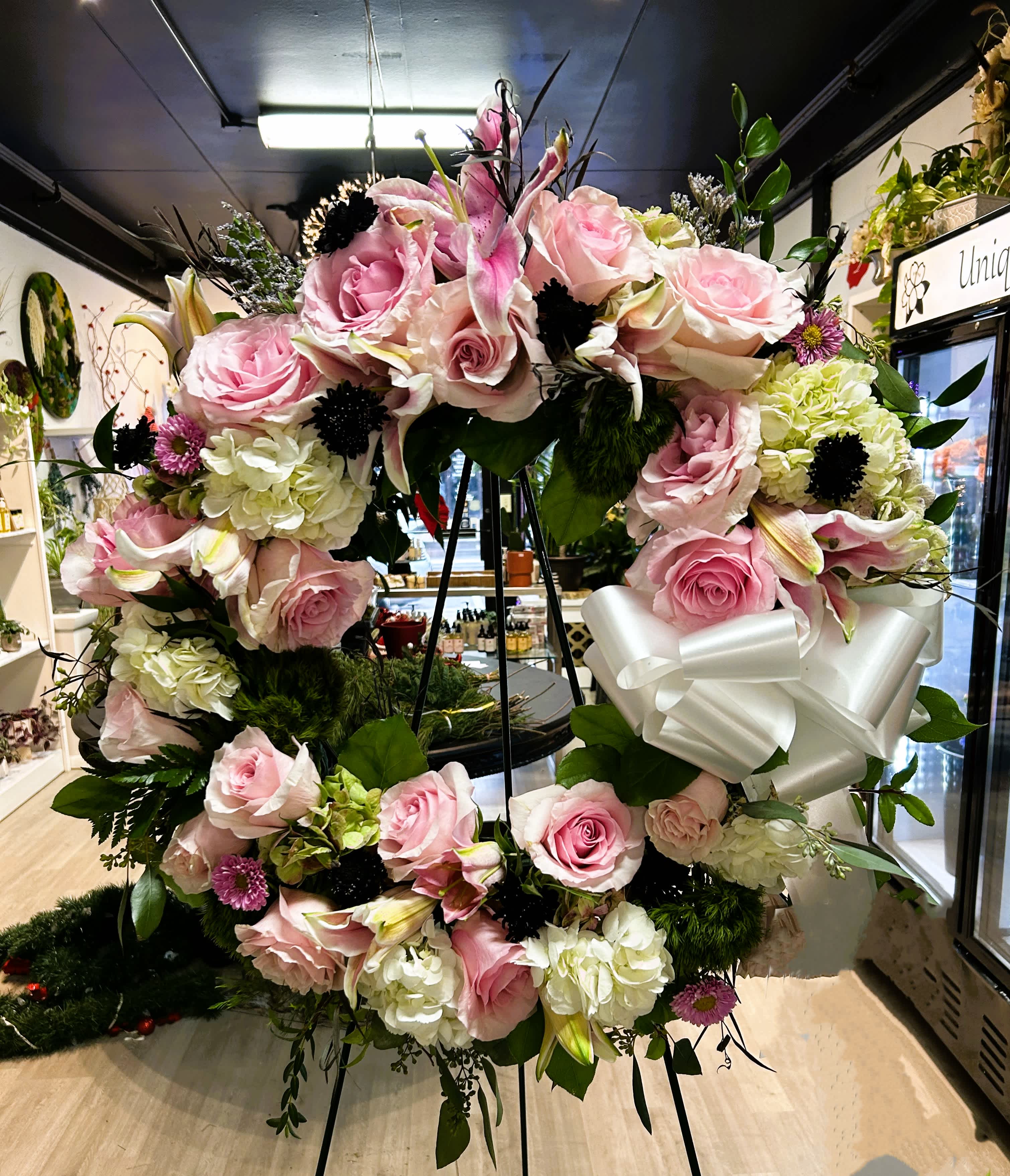 Pink tribute wreath by Unique K Floral Studio - A serene commemoration of a life well-lived and peacefully passed. This tribute wreath, adorned in shades of soft pink and green, is a beautiful celebration of a full and meaningful journey.