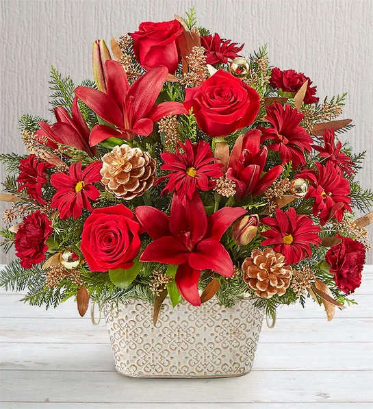 Loving Remembrance Red - Celebrate the life of a loved one during the holiday season with our beautiful floral tribute. A mix of rich red and burgundy blooms, symbolizing enduring love, is gathered with golden ornaments and pinecones for an elegant presentation. Designed in our Remembrance Cachepot, featuring an embossed pattern and finished with a gold brushed ivory surface, it’s a special way to honor their memory this time of year.  One-sided arrangement of red roses, Asiatic lilies and daisy poms, burgundy carnations; accented with seeded eucalyptus, assorted Christmas greenery, gold ball ornaments and pinecone picks Hand-designed in our exclusive Remembrance Cachepot, featuring a comforting embossed pattern and finished with a gold brushed ivory surface, a symbol of purity of heart and enduring love; measures 5&quot;H x 8.5&quot;W Arrangement measures approximately 18&quot;H x 15&quot;W  Appropriate for sending to the service and to the homes of family or friends Our florists hand-design each arrangement, so colors and varieties may vary due to local availability To ensure lasting beauty, Asiatic lilies may arrive in bud form and will fully bloom over the next few days