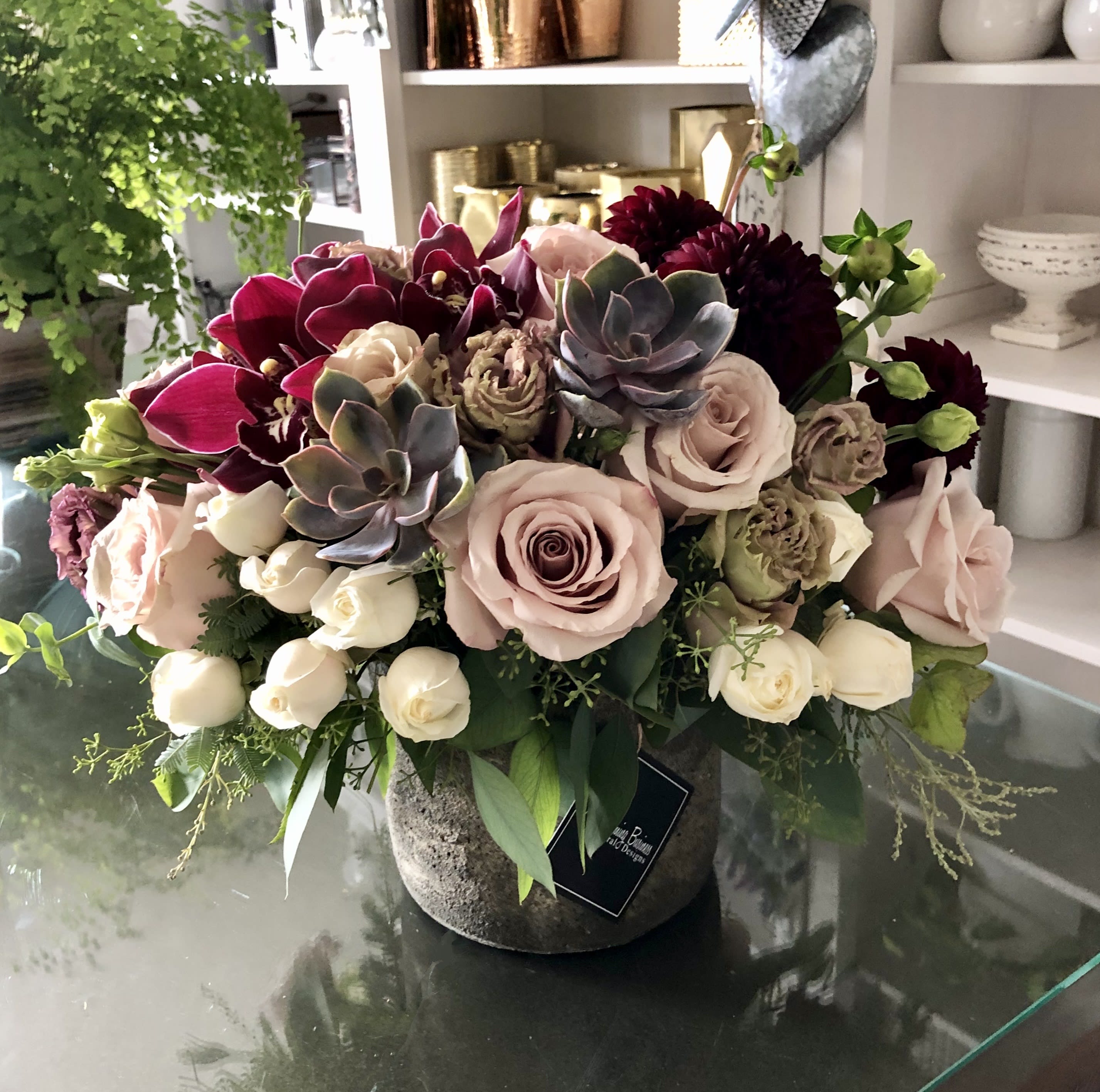 Westlake  - What sets the Westlake Arrangement apart is its versatility. Suitable for any time of the year, this arrangement seamlessly adapts to any decor or ambiance. Its rich burgundy orchids exude passion and allure, symbolizing love and desire. The quicksand roses bring a touch of tranquility and grace, their delicate petals infusing the room with a sense of serenity. Cream roses, the epitome of purity and elegance, add a timeless charm to the ensemble. And finally, succulents introduce a contemporary twist, grounding the arrangement with their unique texture and a touch of modernity. 