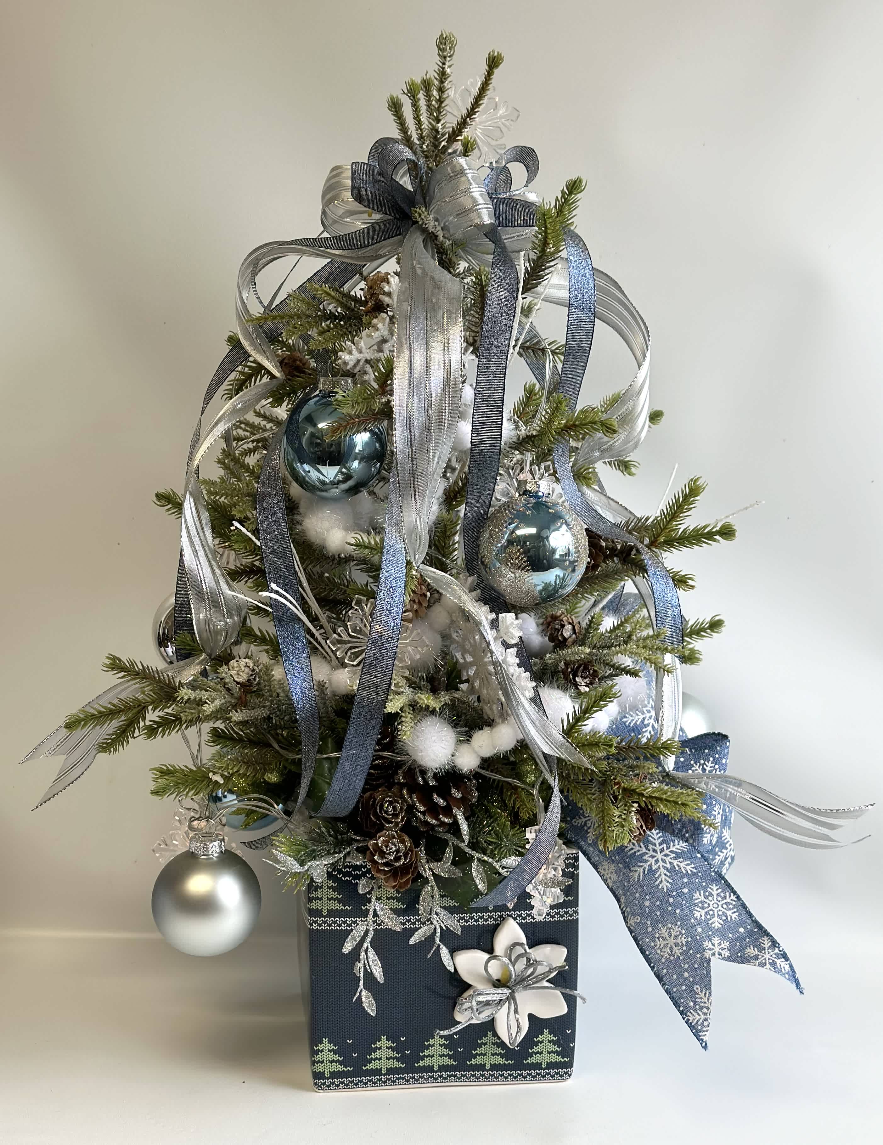 Faux Snowy Christmas Tree Faux Snowy Christmas Tree - Faux Snowy Christmas Tree set in a ceramic container with lights, ornaments and pinecones. Blue, Silver and White