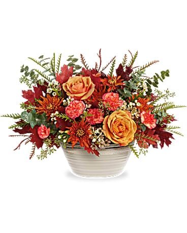 Teleflora's Rustic Harvest Centerpiece - Fresh from the fall countryside, this orange rose centerpiece--arranged in a stunning stoneware bowl with reactive glaze--brings rustic autumnal beauty to any occasion. This bouquet features light orange roses, miniature orange carnations, bronze cushion spray chrysanthemums, white waxflower, spiral eucalyptus and grevillea accented with preserved oak leaves. Delivered in a Rustic Harvest Bowl.
