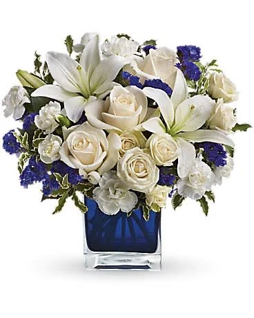 Sapphire Skies Bouquet Sapphire Skies Bouquet - Send someone a bit of heaven with this beautiful bouquet. Luxurious crème roses and pure white lilies paint a peaceful picture inside a sapphire blue cube. Crème roses, white Asiatic lilies, and white miniature carnations are mixed with bursts of purple statice and green pitta Negra. Delivered in a glass Cube.