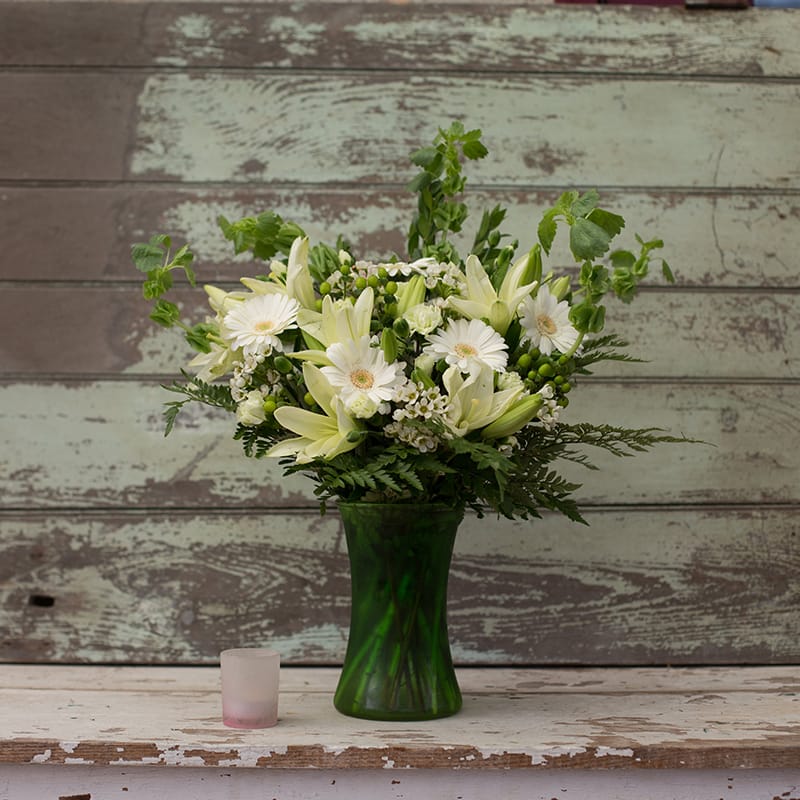 Going Green Going Green - Green and white flowers in a green gathering vase make this arrangement perfect for many occasions. Great for the “Irish Lassie” who loves Bells of Ireland or even perfect as a sympathy arrangement without going “over the top.” White Lilies, white gerbera, mini carns, hypericum berries, bells of Ireland, waxflower and greenery-this one is sure to last!