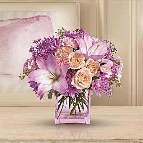 Teleflora's Possibly Pink  *Vase will be substituted* - Impossibly pretty. This decidedly feminine arrangement is absolutely delightful. Perfectly peachy peach spray roses pink asiatic lilies and miniature carnations lavender cushion spray chrysanthemums and waxflower pittosporum and seeded eucalyptus fill an exclusive pink cube. Have one delivered and almost anything's possible.  The bouquet pictured reflects our original design for this product. While we always try to follow the color palette, we may replace stems to deliver the freshest bouquet possible, and we may sometimes need to use a different vase.  