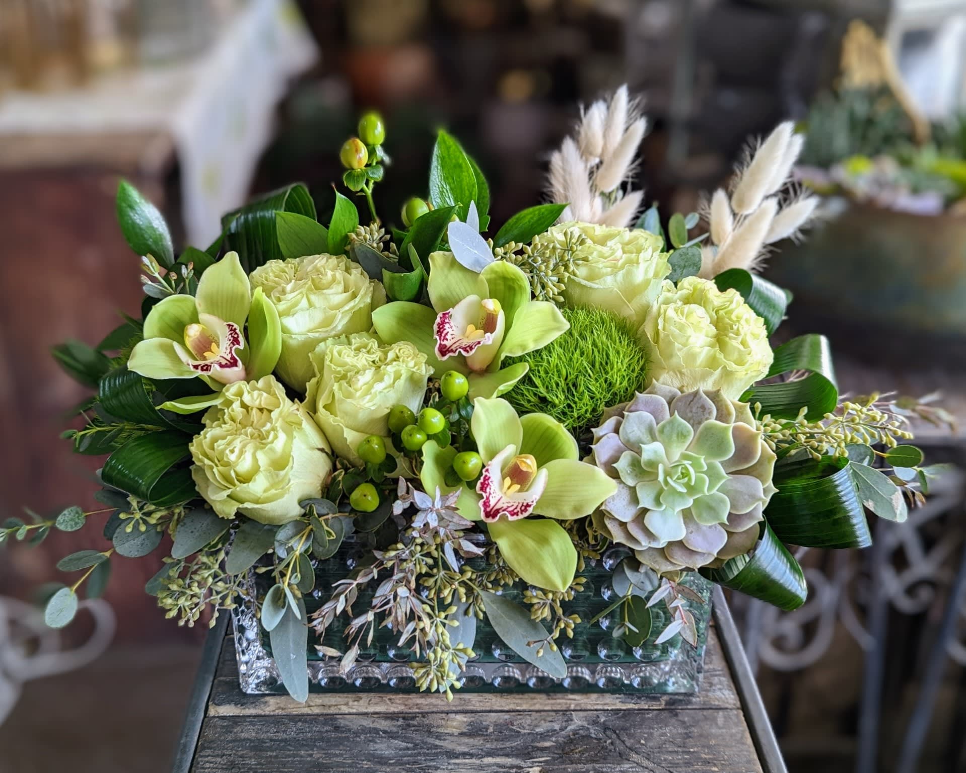 Chartreuse - Roses, orchids, green trick, a succulent, and mixed foliage in shades of green in a glass rectangular vessel.