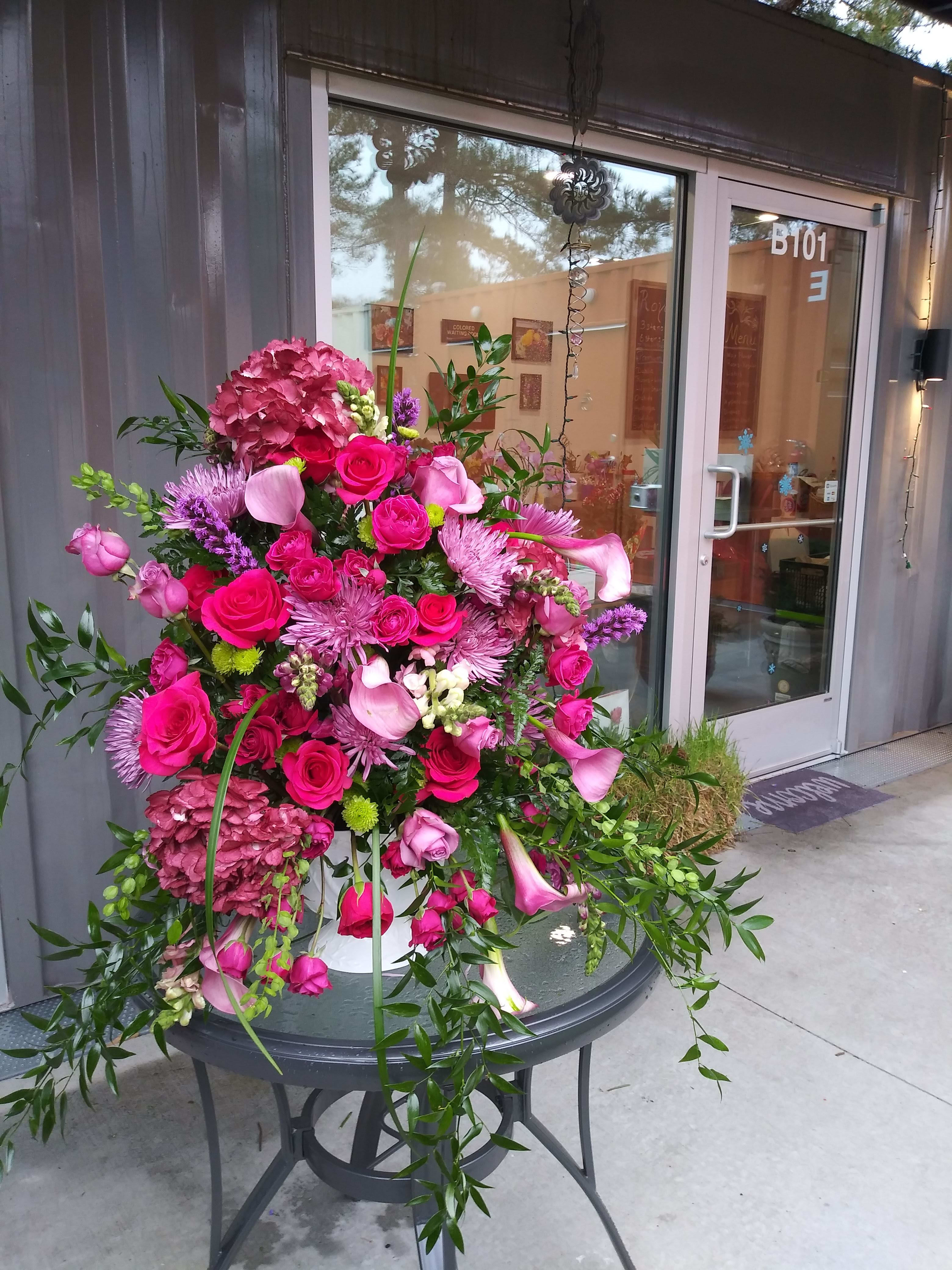 Royal Embrace High Style Basket - An exquisite one-sided display of hot pink Roses and spray roses, hydrangea, spider mums, calla lillies,  green pom poms, purple Larkspur, Itallian ruscus, Myrtle,bear grass and varied assorted filler in greenery in a fan basket