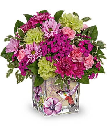 Teleflora's Hummingbird Garden Bouquet - As magical as a walk through a secret garden, this wondrous arrangement of colorful blooms in a vintage garden cube vase will make Mother's Day one to remember. This delightful arrangement features green carnations, miniature pink carnations, purple cushion spray chrysanthemums, lavender sweet william, lavender daisy spray chrysanthemums, pitta negra and lemon leaf. Delivered in a Sweet Hummingbird cube.