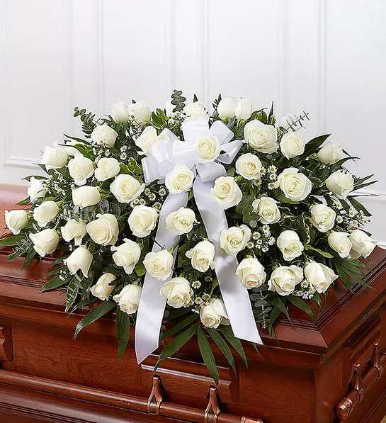 Half Casket Cover - White, Red or Pink Roses - The precious moments spent with loved ones are the moments we want to hold onto forever. Capture this sentiment with a timeless display of all white. Our half casket cover, crafted with care and artistry by our expert florists with over 50 roses, Fillers and accented with a satin ribbon, is an unforgettable way to commemorate a lifetime of shared loving experiences. *** CHOOSE YOUR COLOR ***