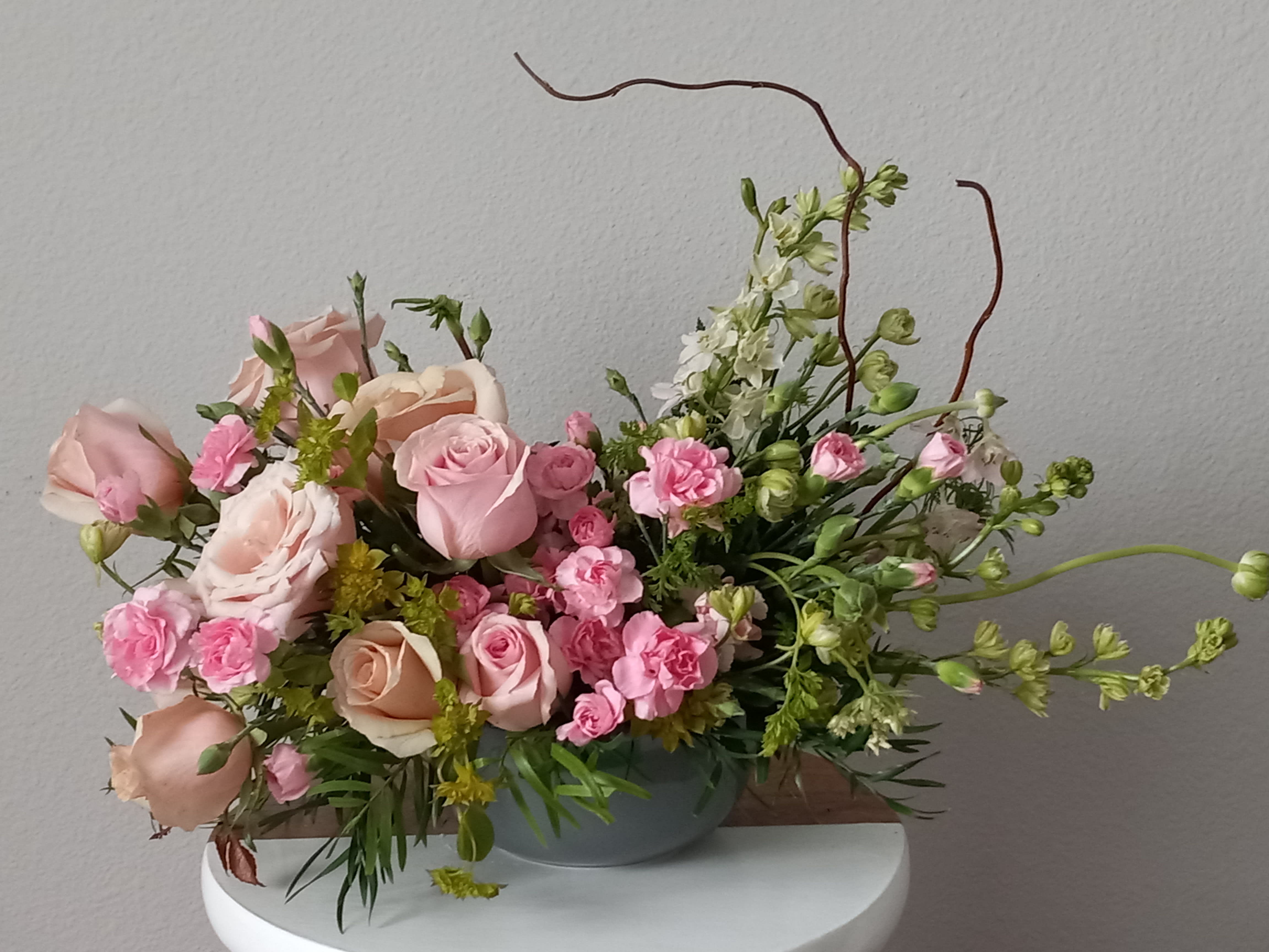 Rosy Iridescence Bouquet - Think pink!  Rosy Iridescence Bouquet features beautiful pink roses, pink mini carnations, pink larspur, pink spray roses in a shimmering, iridescent gray ceramic vase that is sure to love.  Pink roses, pink spray roses, pink alstroemeria and pink rice flower are arranged with leatherleaf fern, pink limonium and silver dollar eucalyptus.   Orientation: All-Around  SUBSTITUTION POLICY – Always deliver the freshest flowers! Please note the bouquet pictured reflects our original design.  If the exact flowers or container in this arrangement are not available, our local florists will create a beautiful bouquet with the freshest available flowers.