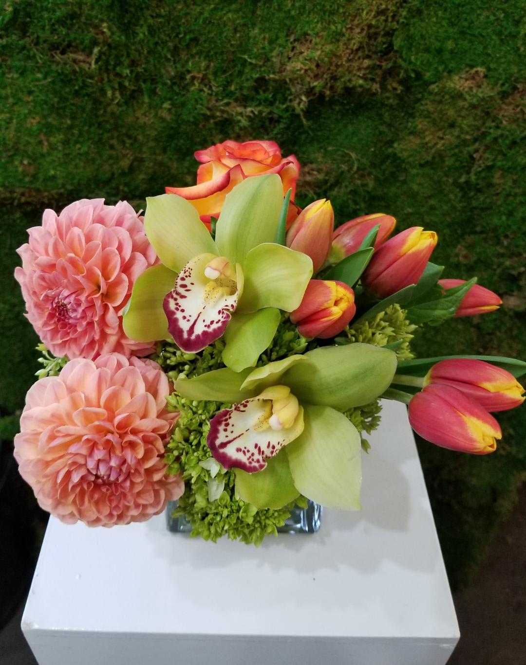 Tango in orange - Say hello with this fun and cheerful arrangement making anyone smile with it's mixture of Roses, Tulips, Orchids and Soft greens to accentuate it's fun character. 