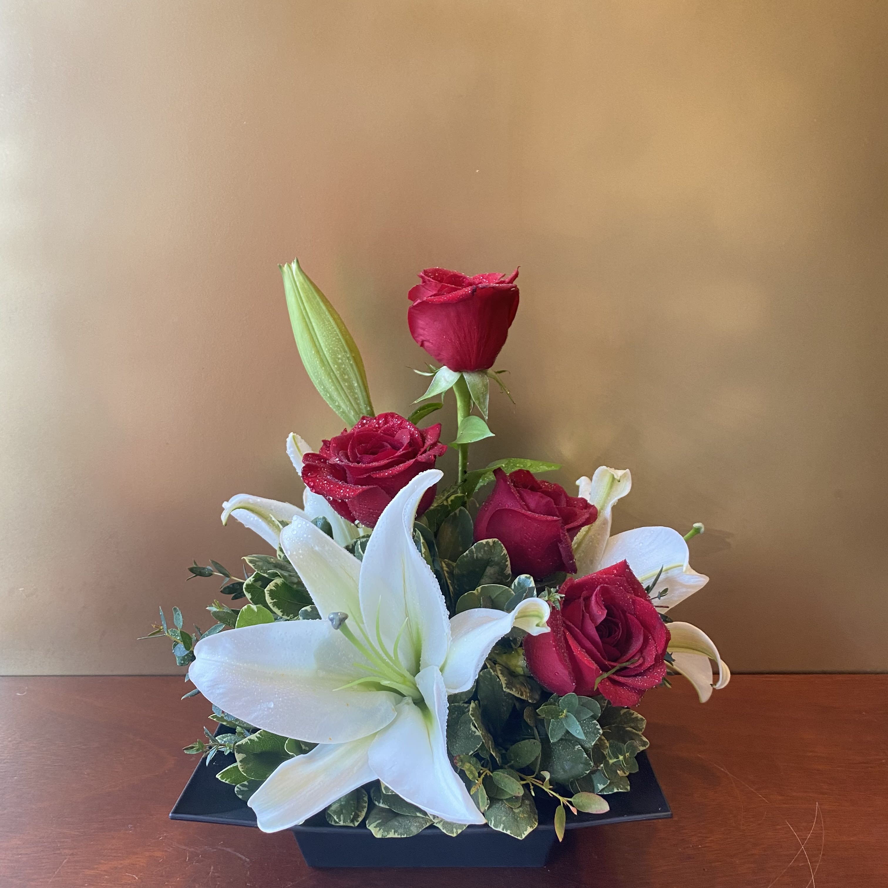 Full of Grace - This graceful arrangement of soft red and whites is quite a show stopper! Full of Grace combines white oriental lilies, red roses and tropical greens are arranged in a square design dish . No matter what the occasion, this is the perfect gift!