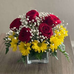Simply You - This is a classic red rose bouquet, but with a twist, this enchanting arrangement is sure to bring a smile. Bright enlightening yellow margarita flowers surround the couple of red roses. For a touch of freshness Baby’s Breath and leather leaf ferns are added. Everything is creatively arranged in an elegant square vase.