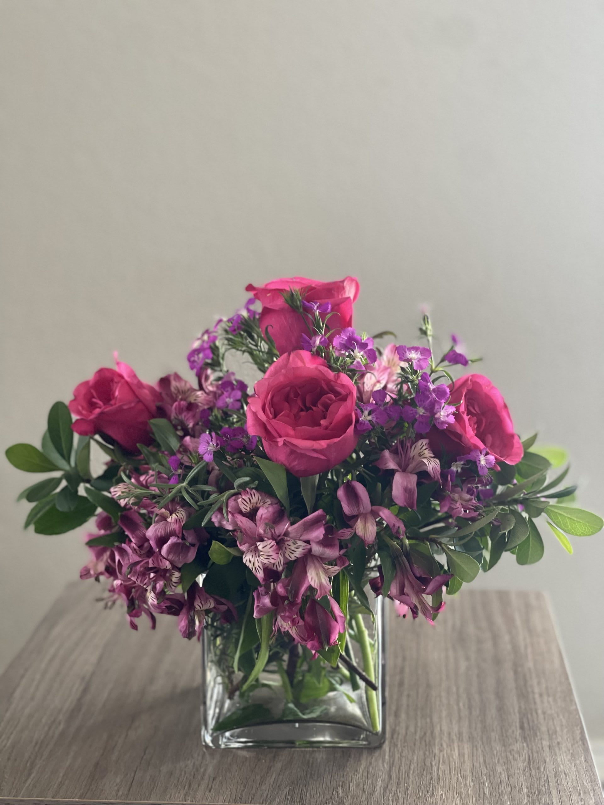 Raspberry Ripple - This exquisite floral arrangement features a delightful combination of fuchsia roses, purple alstroemeria flowers, and purple dianthus, complemented by fresh greens. The vibrant colors and elegant blooms create a visually stunning display that will captivate any recipient. The arrangement is beautifully presented in a clear square vase, adding a modern touch to its overall charm. Perfect for any occasion, this floral masterpiece is a thoughtful gift that will bring joy and beauty to any space.