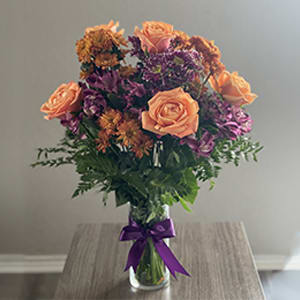 Autumn Radiance Bouquet - Beautiful bouquet of orange roses, purple alstroemeria, chrysanthemum flowers with leather leaf all around in a clear vase with an elegant bow.