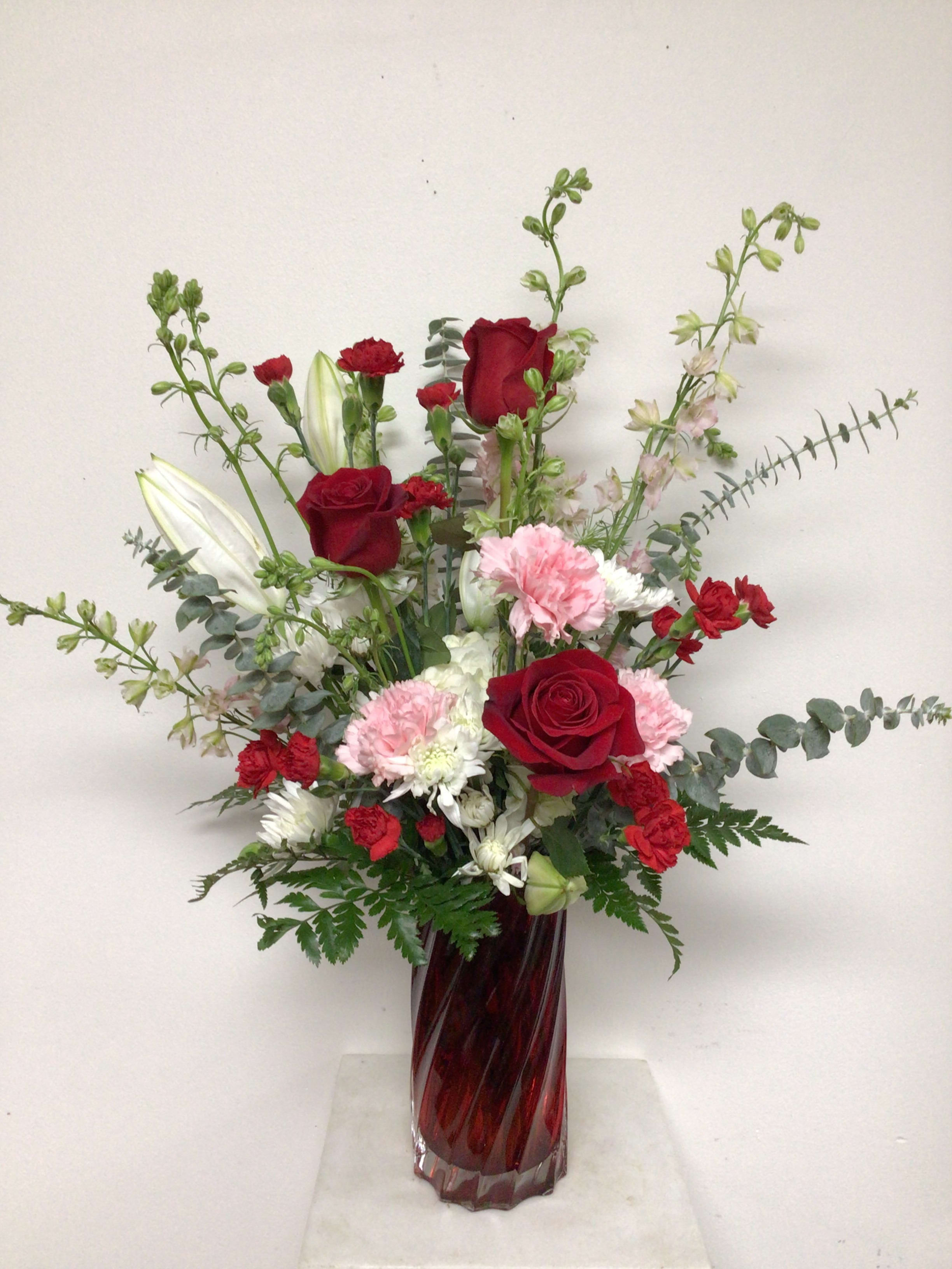 Be Mine - 8 inch tall red glass swirl vase is arranged with white hydrangea, red roses, pink carnations, pink larkspur, white cushion mums, red miniature carnations and spiral eucalyptus. Approximate size is 23 inches tall x 15 inches wide.