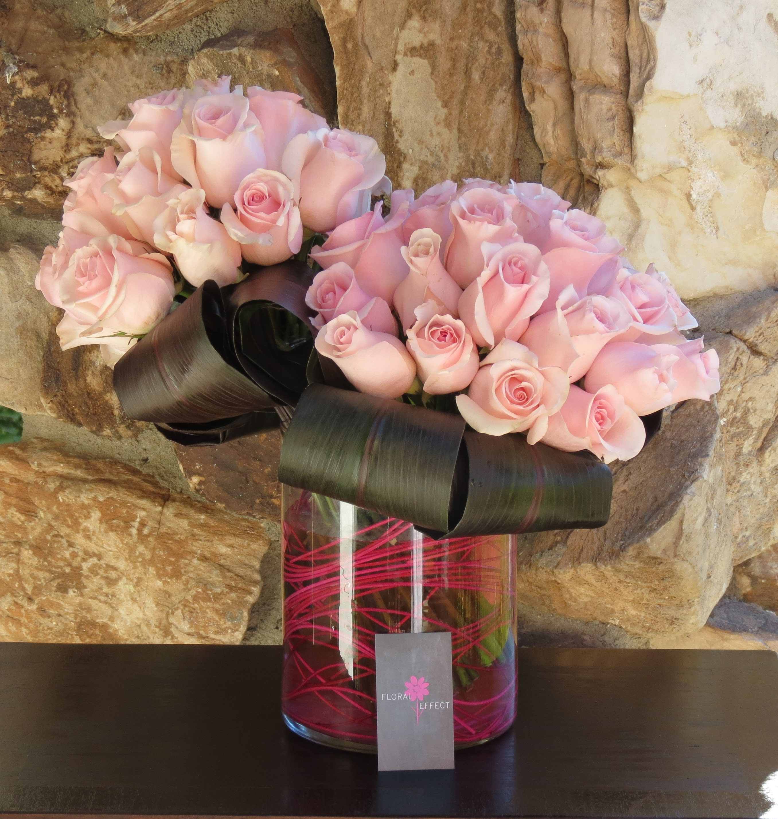 Light Pink Roses - 50 Roses and tropical leaves arranged on a glass vase with pink bamboo accents. Available in more colors. 