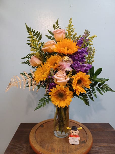 "Stacy's Choice" Bouquet "Stacy's Choice" Bouquet - Introducing 'Stacy's Choice' Bouquet – a radiant burst of sunshine and elegance. Embrace the warmth of sunflowers, the soft allure of peach roses, and the regal touch of purple stock, all harmonized by the golden accents of solidago. A choice that speaks volumes, crafted to bring joy and beauty into every moment.