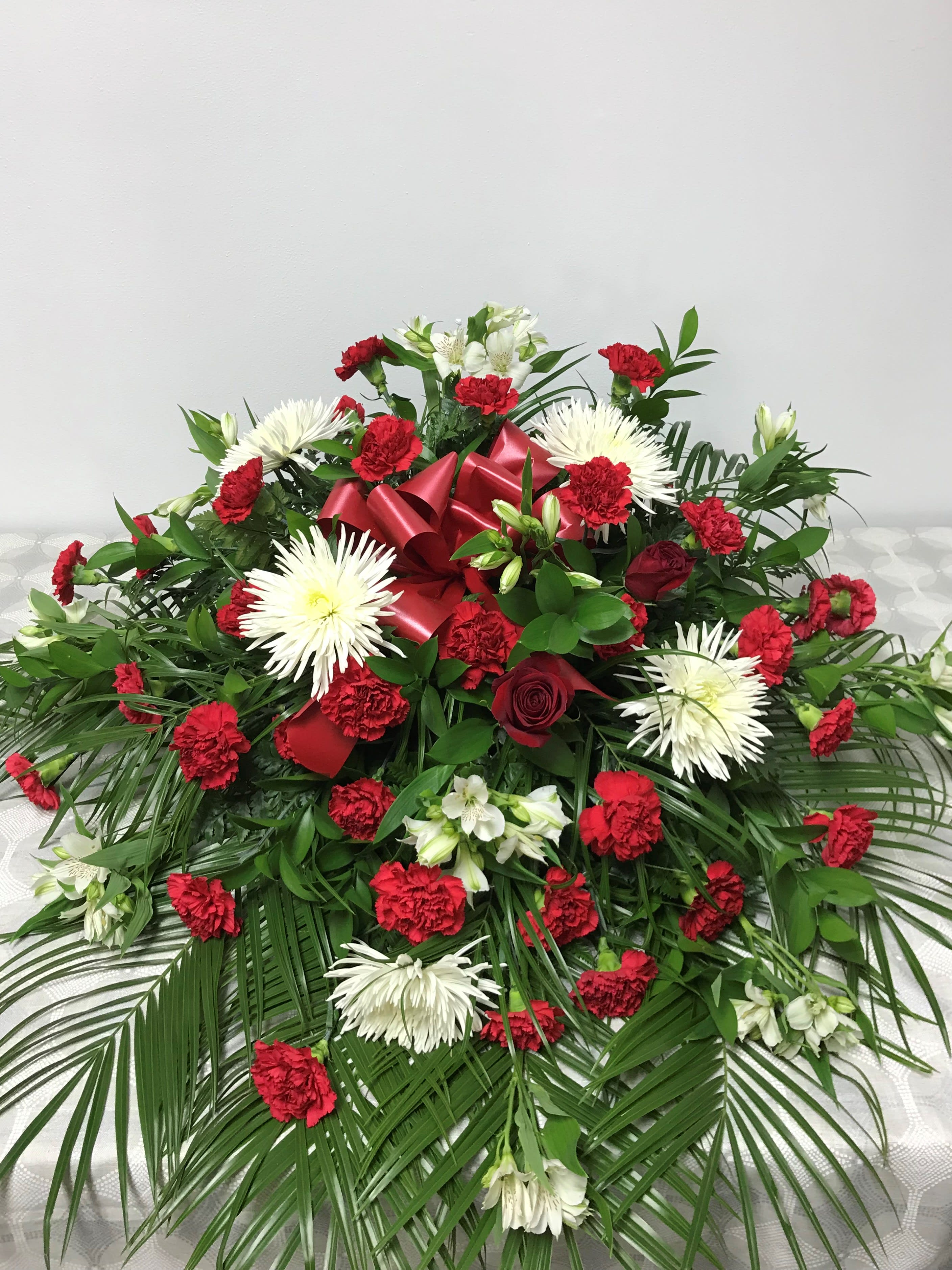 Graceful Casket Spray  - A meaningful and sincere way to honor a loved one, is with an elegant half casket spray.  Exquisite red and white flowers elegantly drape the casket, while serving as a beautiful tribute during their final service.