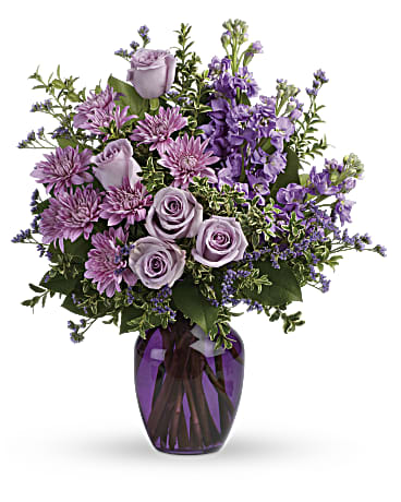 Together At Twilight Bouquet - The perfect pick for the purple lover in your life! This impressive bouquet charms with roses, stock and mums. Presented in a gorgeous glass vase. This dramatic arrangement includes lavender roses, lavender stock, lavender cushion spray chrysanthemums, lavender limonium, oregonia and lemon leaf. Delivered in a purple glass vase. Orientation: All-Around