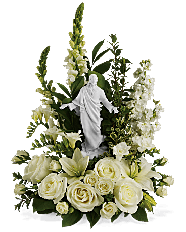 Eckert Florist's Teleflora's Garden of Serenity Bouquet - This serene, all white bouquet features a porcelain likeness of Jesus designed by famed artist Stuart Mark Feldman. A sacred choice to send. The religious arrangement evokes divine grace and Christian purity. White flowers such as roses, asiatic lilies, stock and/or snapdragons are accented with lush greens around a porcelain Sacred Grace keepsake figure. Orientation: One-Sided 