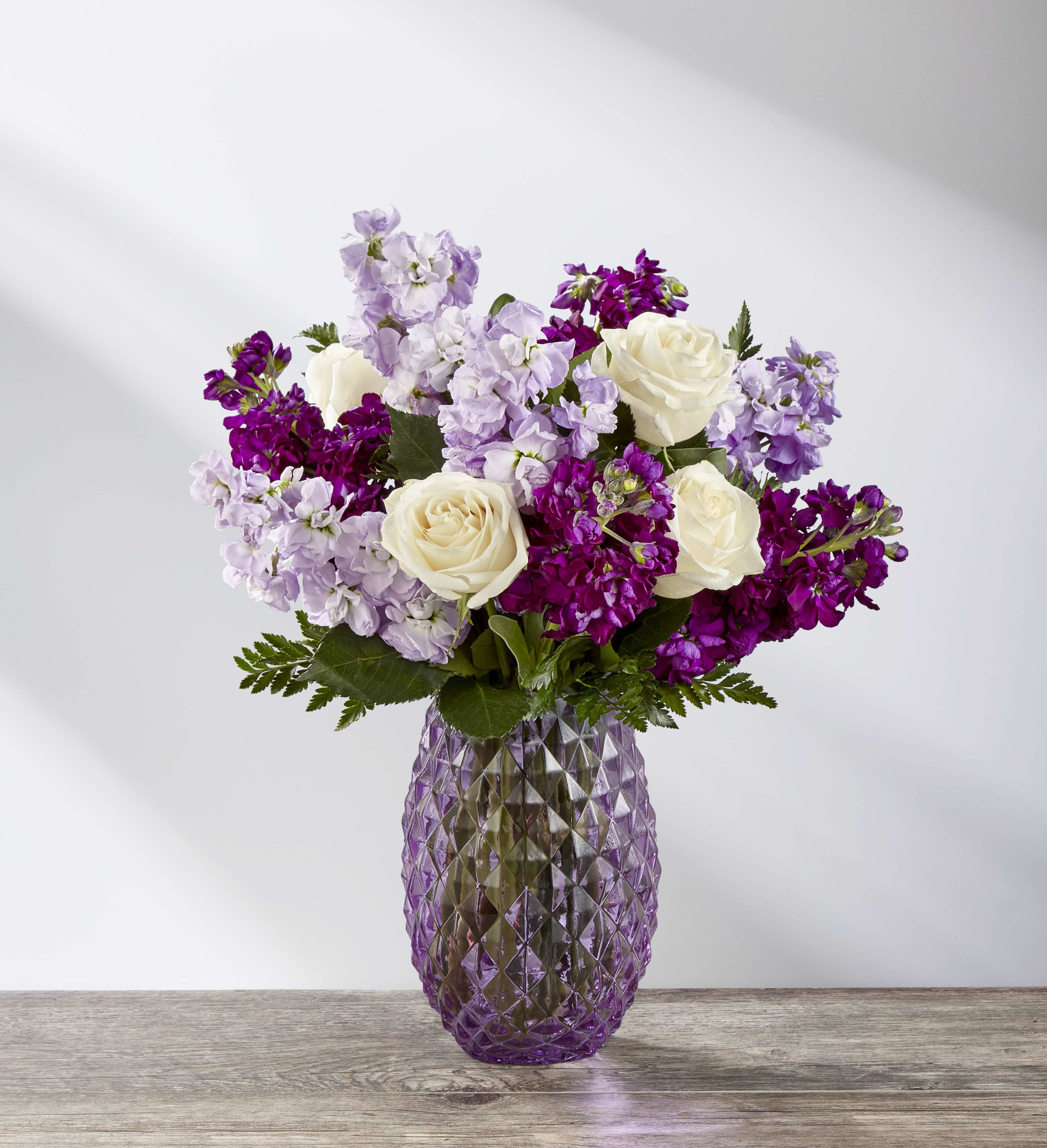 The FTD® Sweet Devotion™ Bouquet - The FTD® Sweet Devotion™ Bouquet is a bold blend of modern color and style to create an exceptional springtime gift, this fresh flower arrangement is ready to surprise and delight your special recipient! Columns of purple and lavender stock, known for their sweet and alluring scent, are brought together with the swirling petals of white roses and accented with lush greens to create a fresh flower bouquet full of impact and grace. Paired perfectly with a keepsake lavender glass vase with a diamond pattern that your recipient will use over and over again, this spring flower bouquet is a wonderful Easter, Mother's Day, Thank you, or Thinking of you gift.