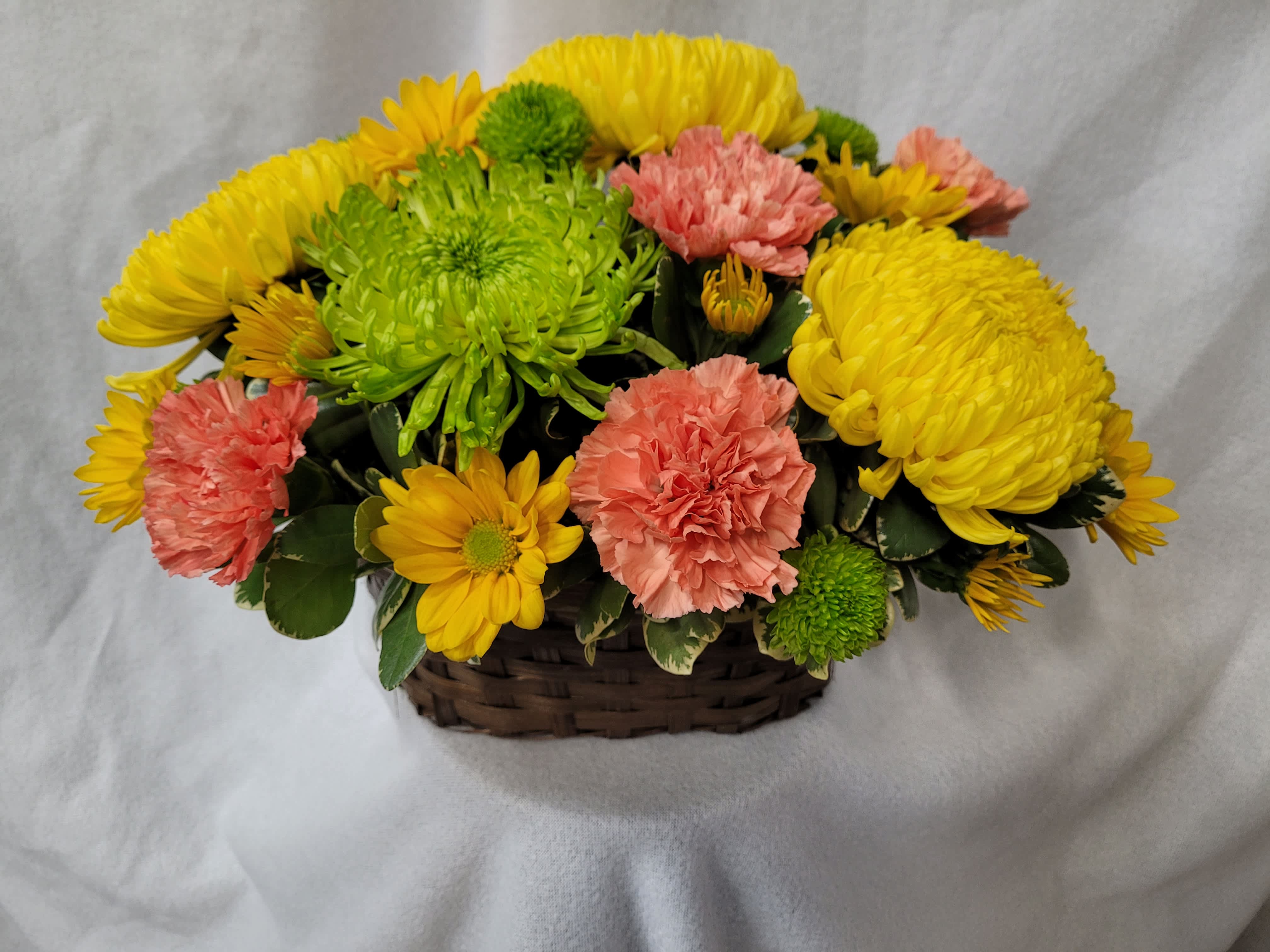 A Basket of Sunshine - This oval basket contains yellow cremones, green spider mum, yellow daisies, green daisies and orange carnations.