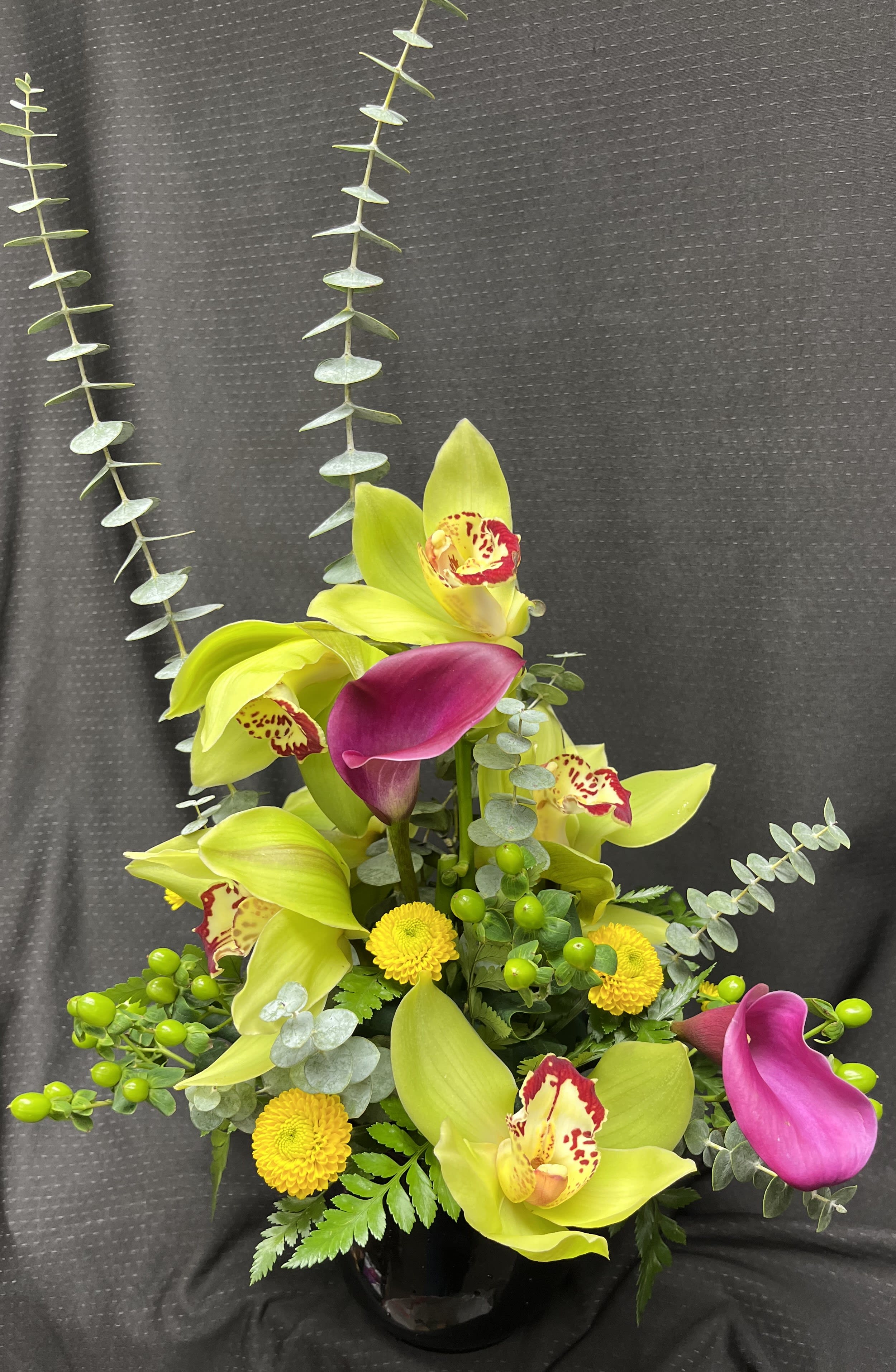 Tropical Oasis  - This arrangement is made up of eucalyptus, orchids, calla lily, and hypericum in a low container.