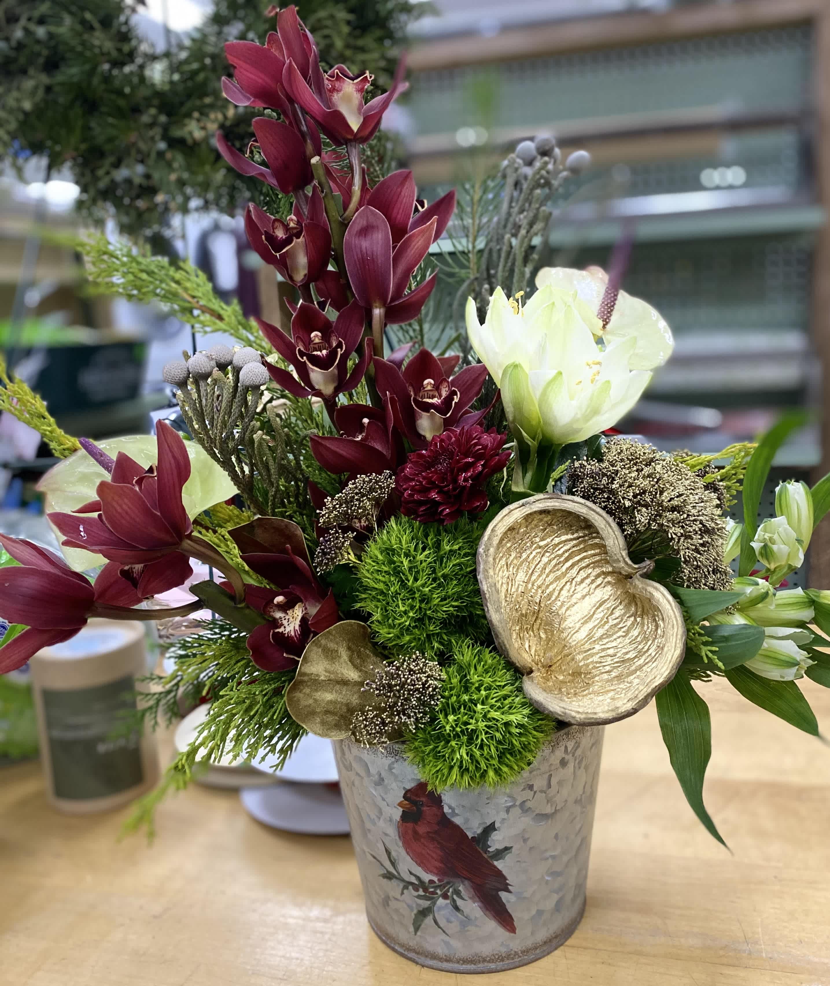 Burgundy   - Winter arrangement made with orchids, peace lily, and roses in a decorative tin. 