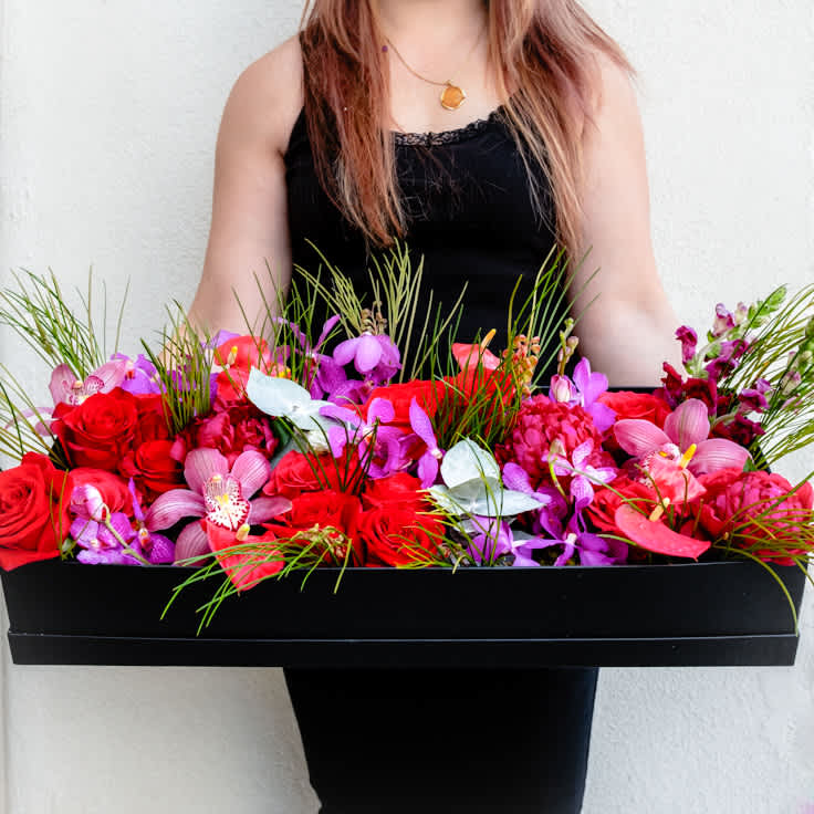 Purple Luxe Box - Luxury redefined in this rectangular box full of all the beauty and elegance nature can provide! This bouquet with warm tones of purple hues florals in the line of cymbidium and molars orchids, peonies, red anthurium, tulips, roses and exquisite greens unveils the blooms meticulously arranged to captivate and indulge, guaranteed!