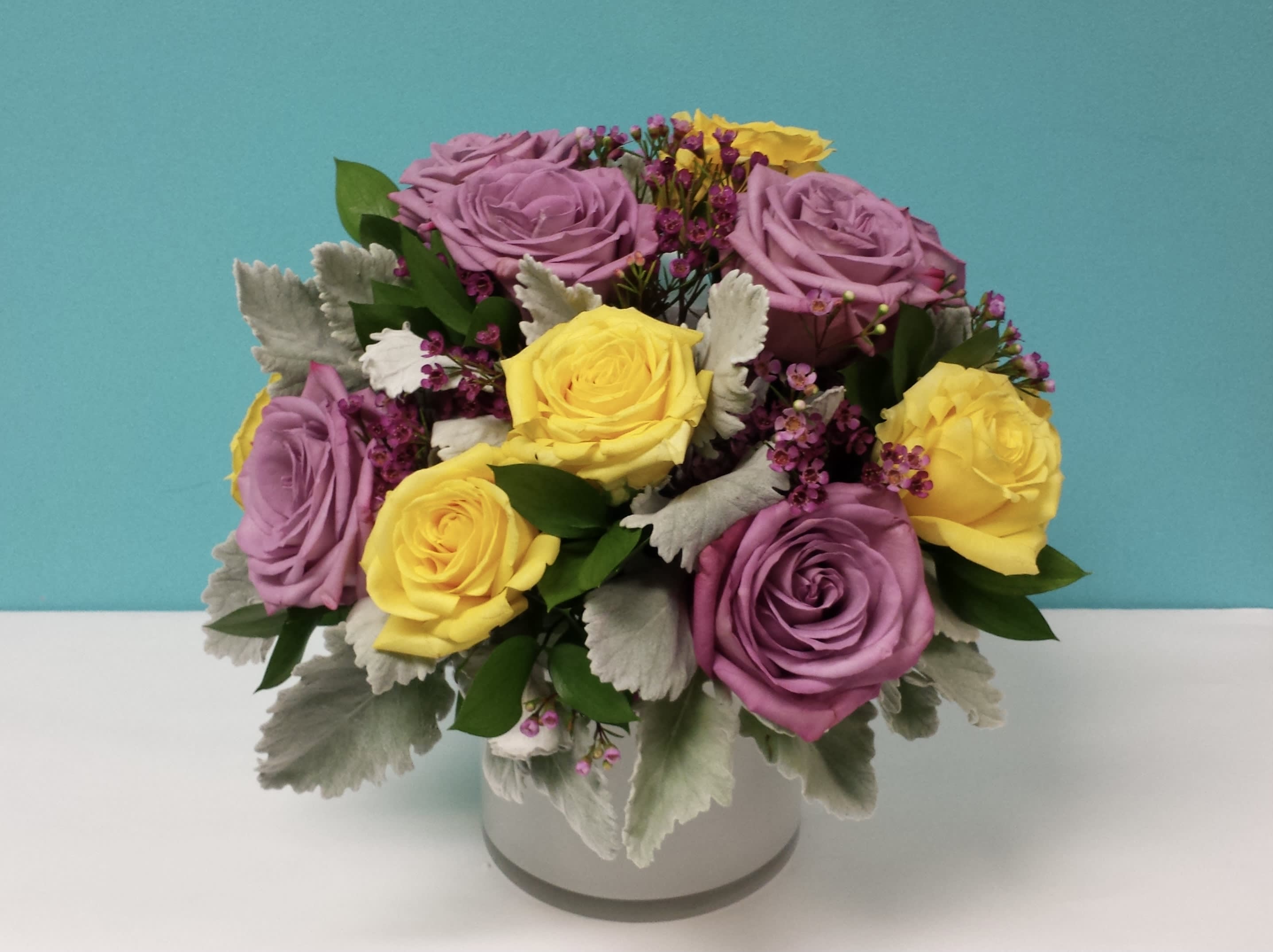 Purple &amp; Yellow Feelings - White clear round vase with roses, dusty miller and other fillers to complement the design.