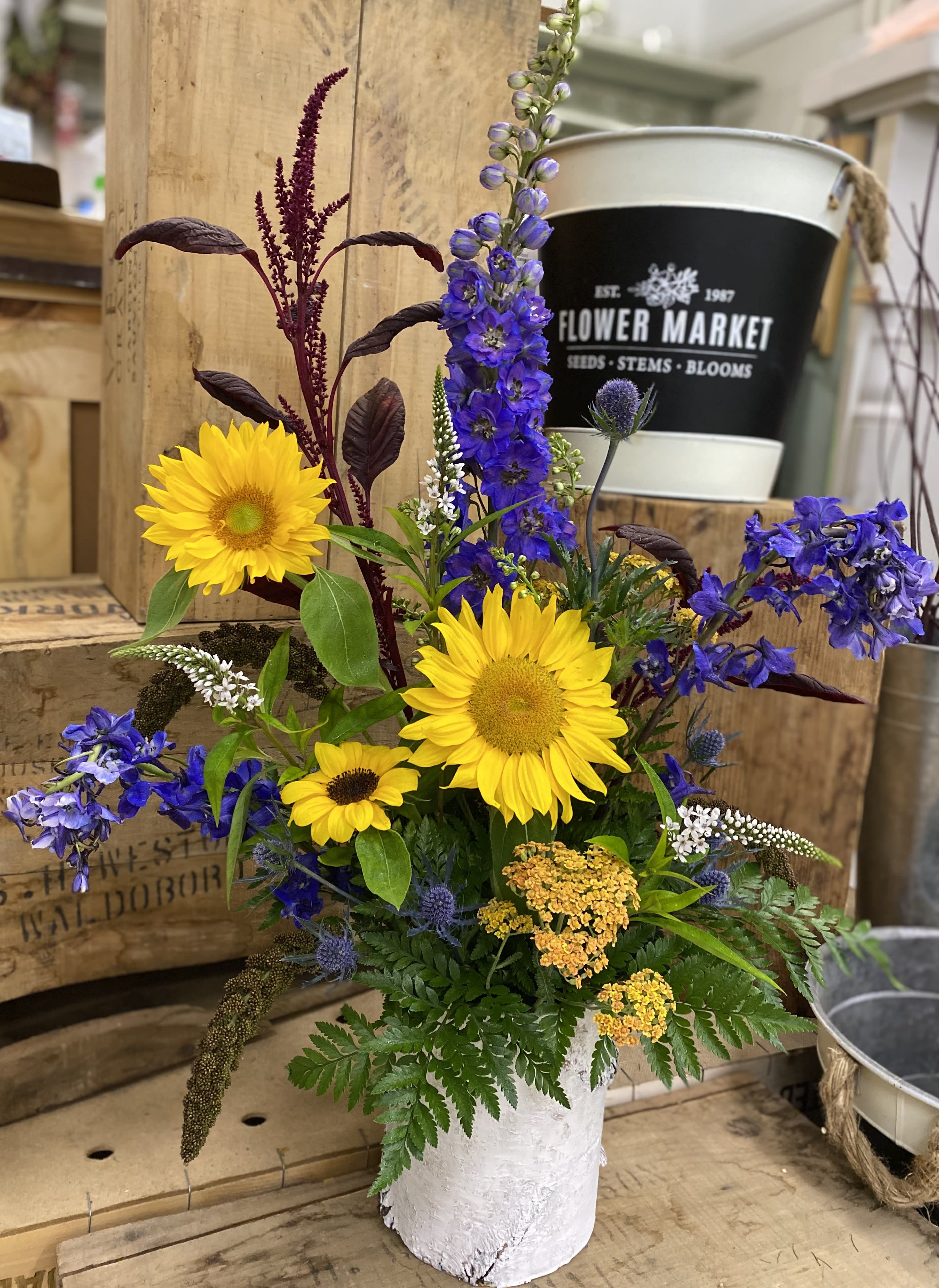 Summer Sun - Tall vase arrangement with delphinium, and sunflowers, in a birchwood container. 