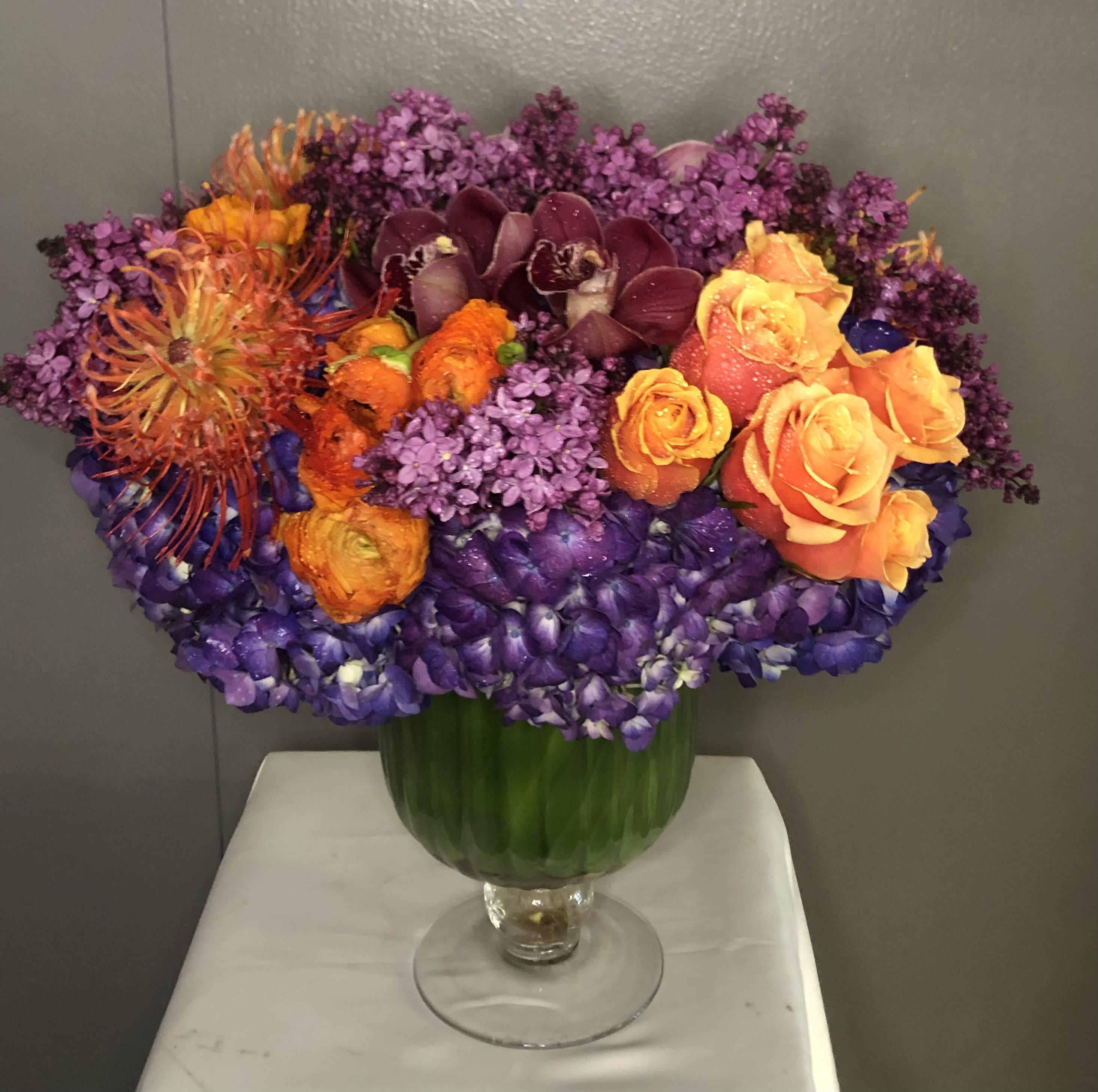 Penelope# EF102 - Fantastic color combination of Roses, Hydrangea, Pin-Cushion, Lilac (seasonal) Ranunculus &amp; orchid in a Designer glass vase
