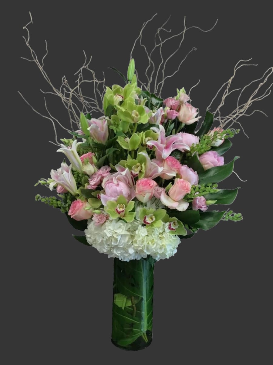 PASTEL LOVE PASTEL LOVE - mix of pastel flowers in a tall cylinder vase. A mix of pink stargazer lillies, green cymbidium orchids, pink roses, white hydrangeas, curly willow, monstera leaves, exoyic foliage, pink spray roses.