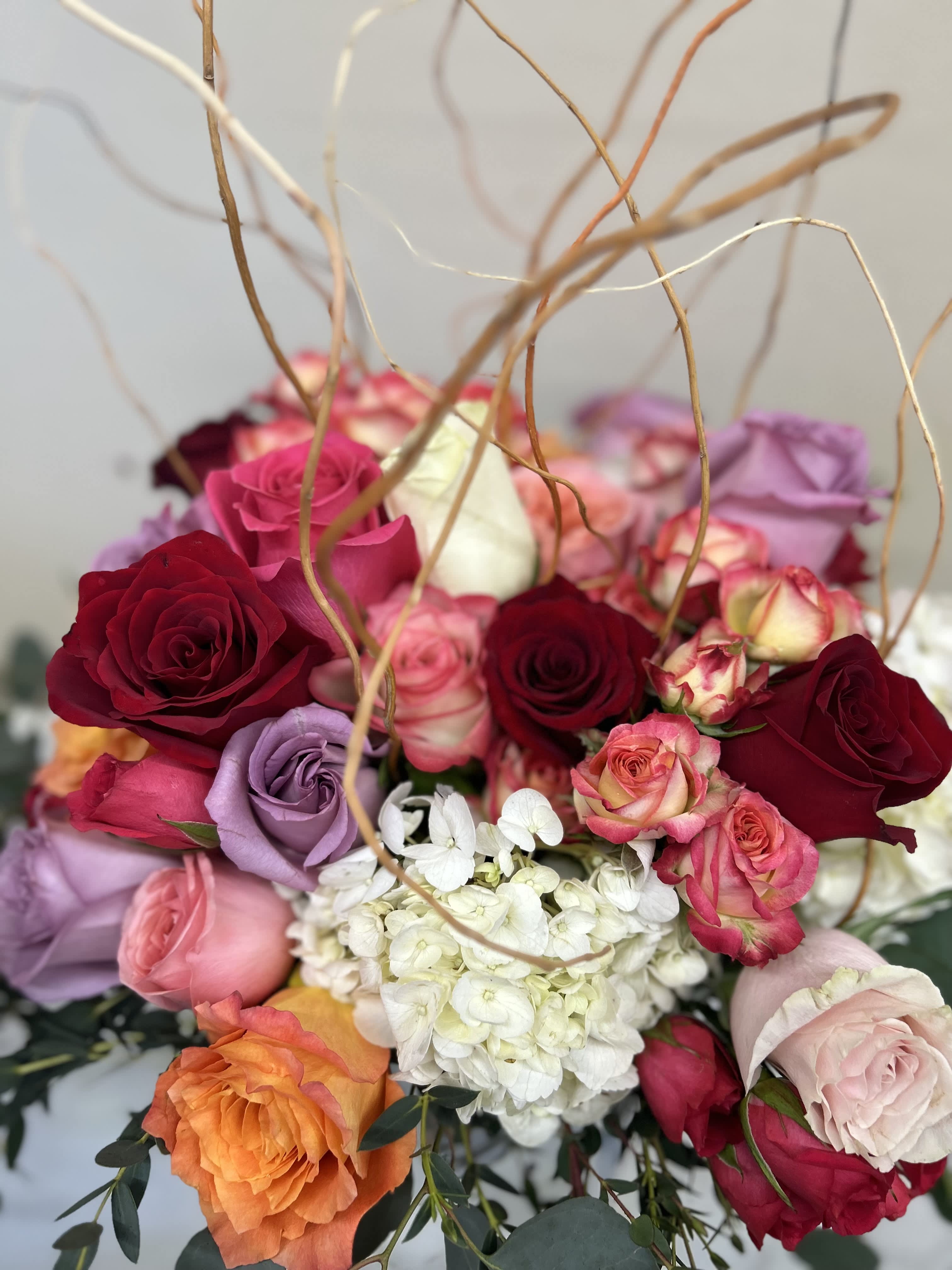 Roses, hydrangeas curly willow, tightly compact in low vase - Mixed color roses red ,purple, pink, orange with hydrangeas and curly willow arranged tightly in a vase