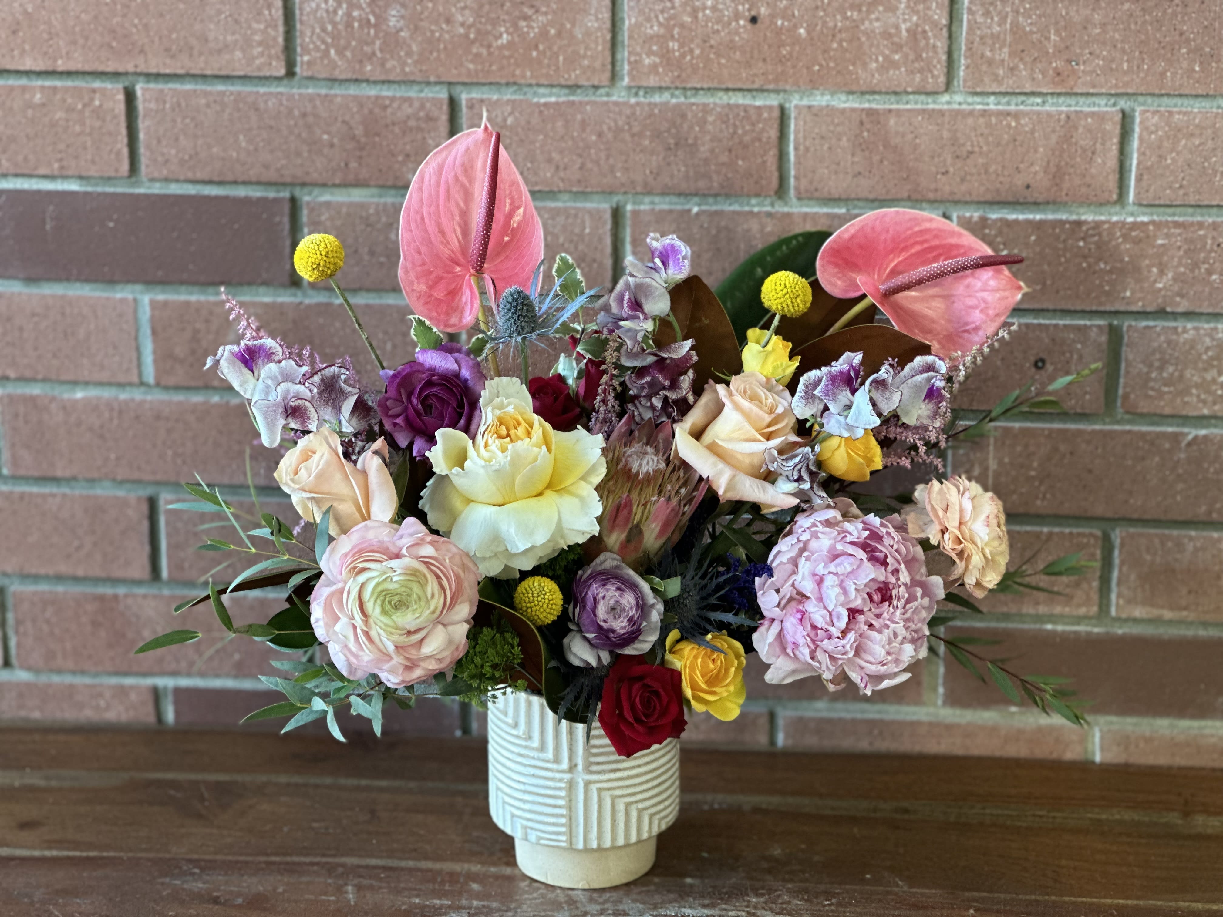 Lush Bold Bouquet  - Modern bold blooms - anthuriums, pink protea, sweet peas, garden roses, ranunculus, peonies, magnolia, astilbe, spray roses, yellow pops and more in a modern ceramic vase. 