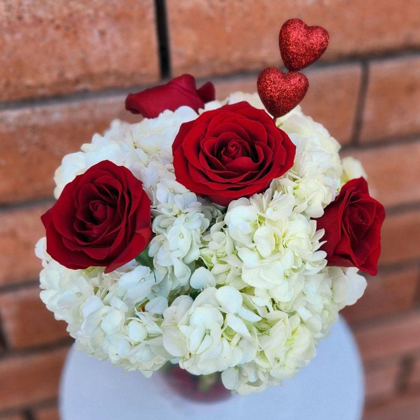 Hearts On Fire - This beautiful arrangement features four premium red roses and three white hydrangeas. Accented with two red hearts and designed in a clear glass vase with red gems. Overall size is approximately 8in (W) x 13in (H).  Care Tips: Place your bouquet in a cool location. Don't put the arrangement in direct sunlight, near heating or cooling vents, in drafty places, directly under ceiling fans, or on top of televisions or radiators. Check water level daily, keep the vase full with clean water. Change water every 2-3 days and apply a sharp fresh cut to the stems. This process will ensure extended flower's life span.