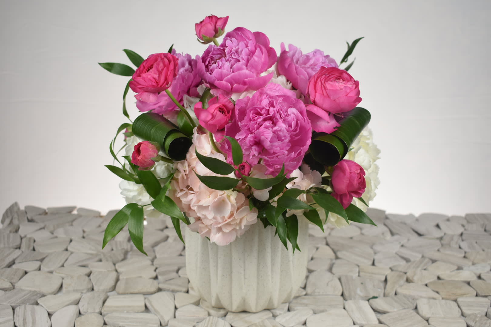 Ranunculus & Peonies Ranunculus & Peonies - This cute lovely arrangement come in a ceramic vase Arranged with light pink Hydrangeas, Pink Peonies, Pink Ranunculus all well combined with some folded aspidistra leafs and greenery. Perfect For any occasion.
