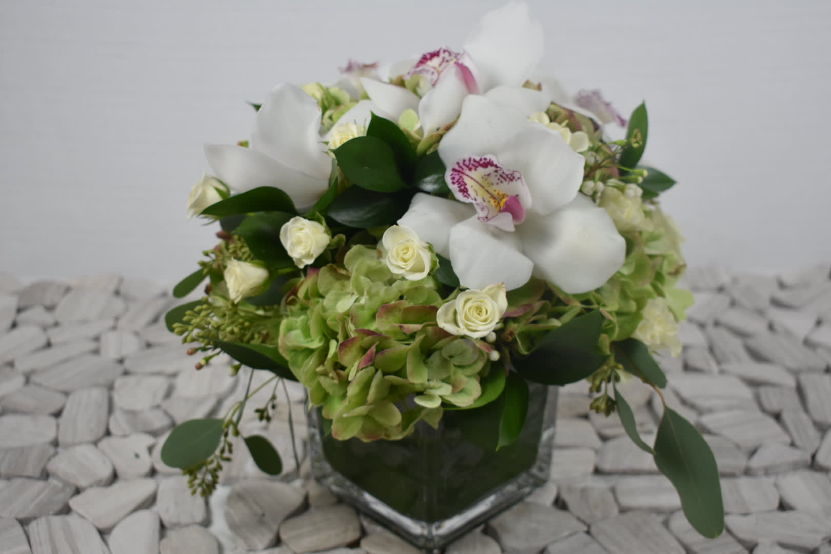 Green Amethyst - This cute little arrangement is perfect for a desk  it comes in a square glass vase with some lovely green hydrangeas, a touch of greenery, white cymbidium orchids, and the perfect touch of white spray roses.  Its just perfect for any occasion 