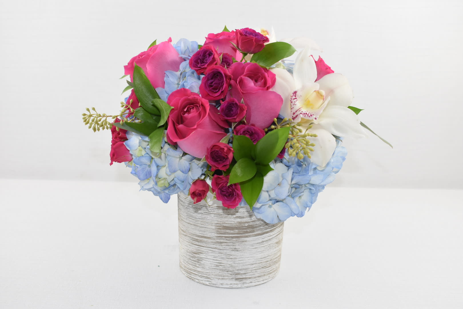 Wow Blue  - Nice cylinder vase with some beautiful blue hydrangeas and some fresh pink Ecuadorian roses with a perfect touch of hot pink spray roses combined with some lovely greens to make this arrangement just the perfect gift we've also added a touch of white cymbidium orchids the right size for an office desk  