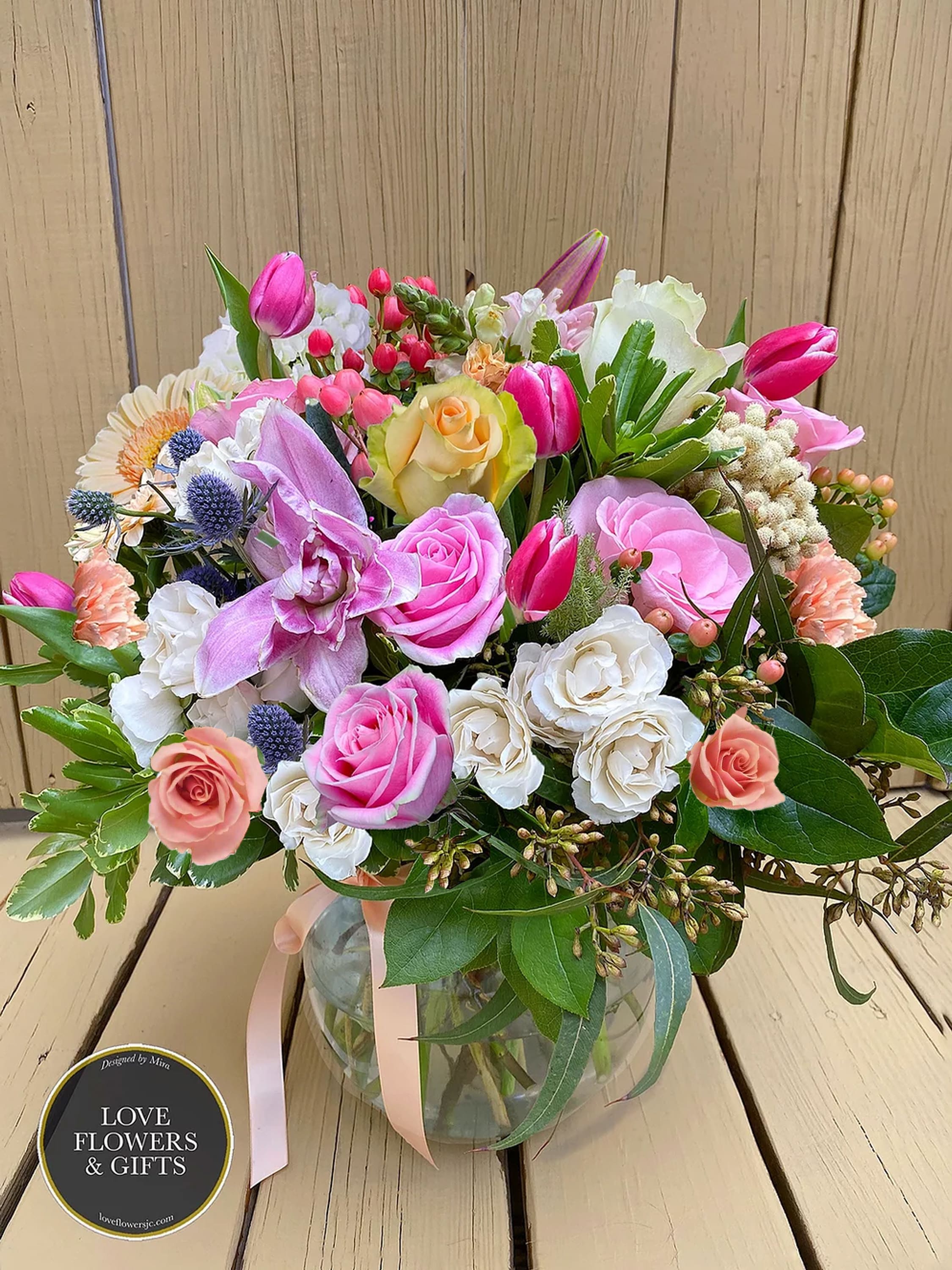 Spring's Blessing - Large, round-style beautiful arrangement of Spring's soft and bright colors in a large high-quality round glass vase with a peach satin ribbon. Includes seasonal flowers. 