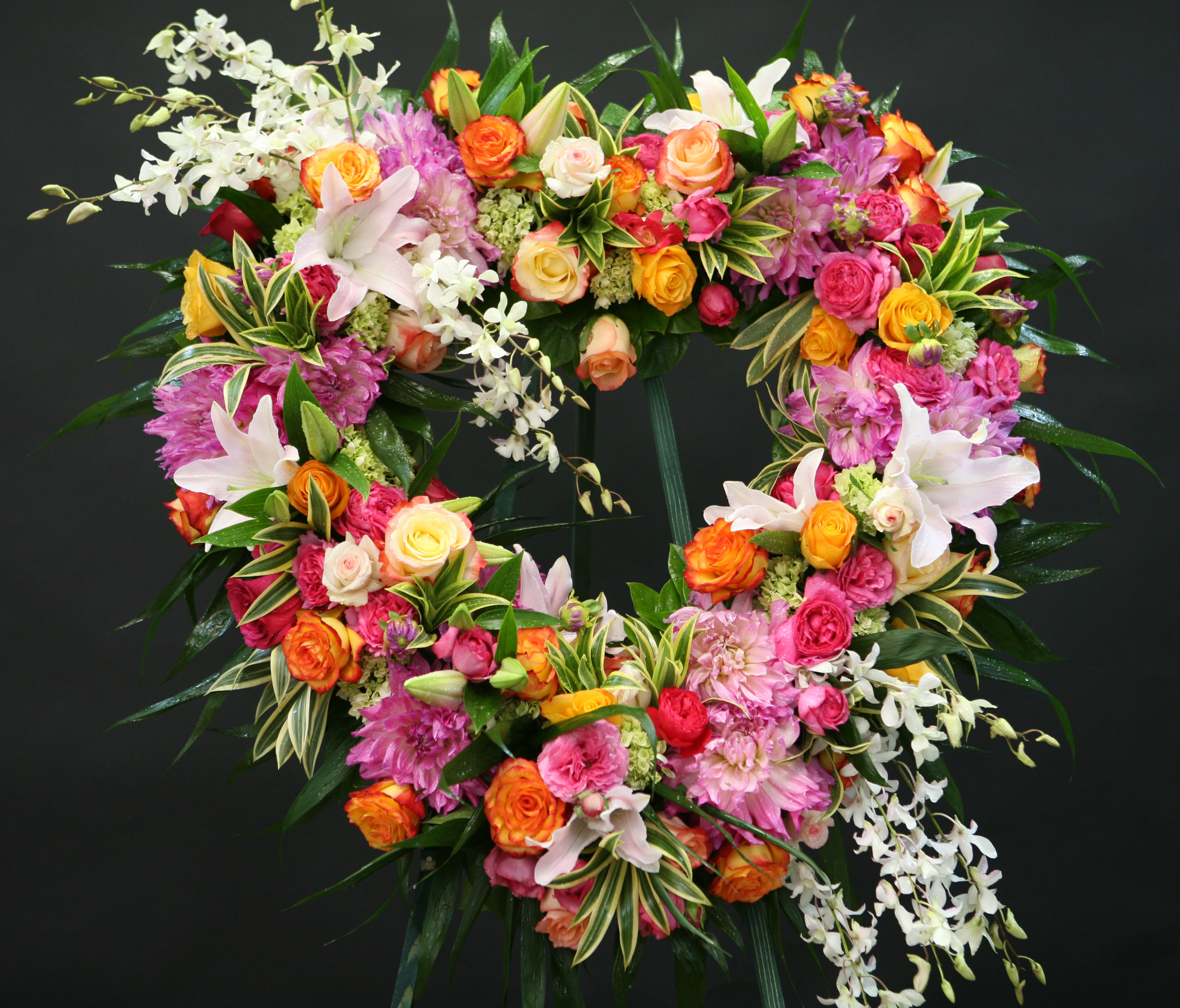 Spirited Heart Wreath with Roses, Lilies &amp; Orchids - An assortment of white, orange, and pink florals in a heart-shaped wreath. May include roses, lilies, dendrobium orchids, dahlias, hydrangea and mixed greens.
