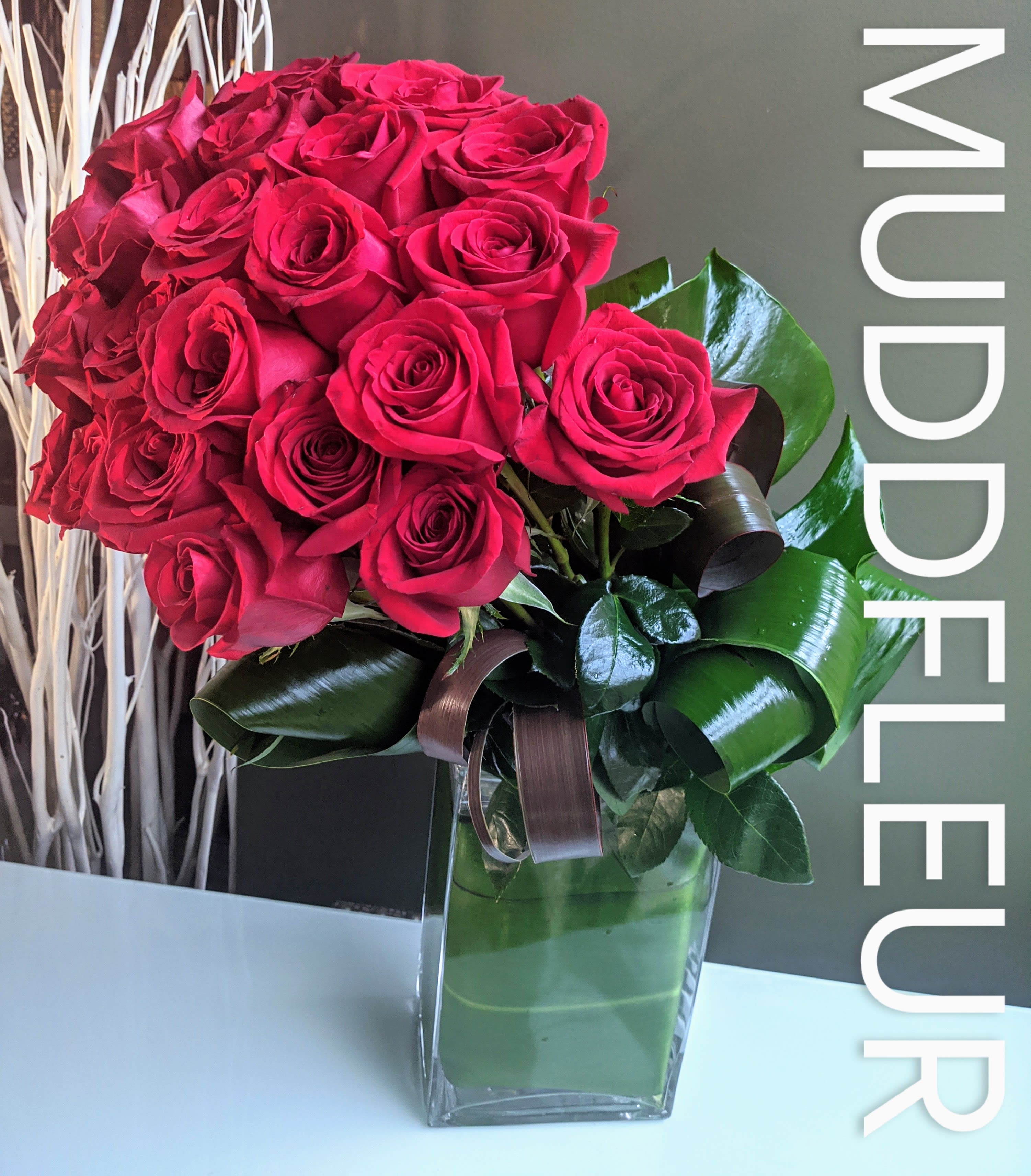 Ruby Red Modern Rose Design  - Ditch the grocery store flowers and send a modern arrangement of red roses from ecuador.  The mudd roses always feature tropical foliages and artistically curled leaves. 12 beautiful roses, available in many colors. Call to see about availability.   All Roses are also available in Round Pave Style!  
