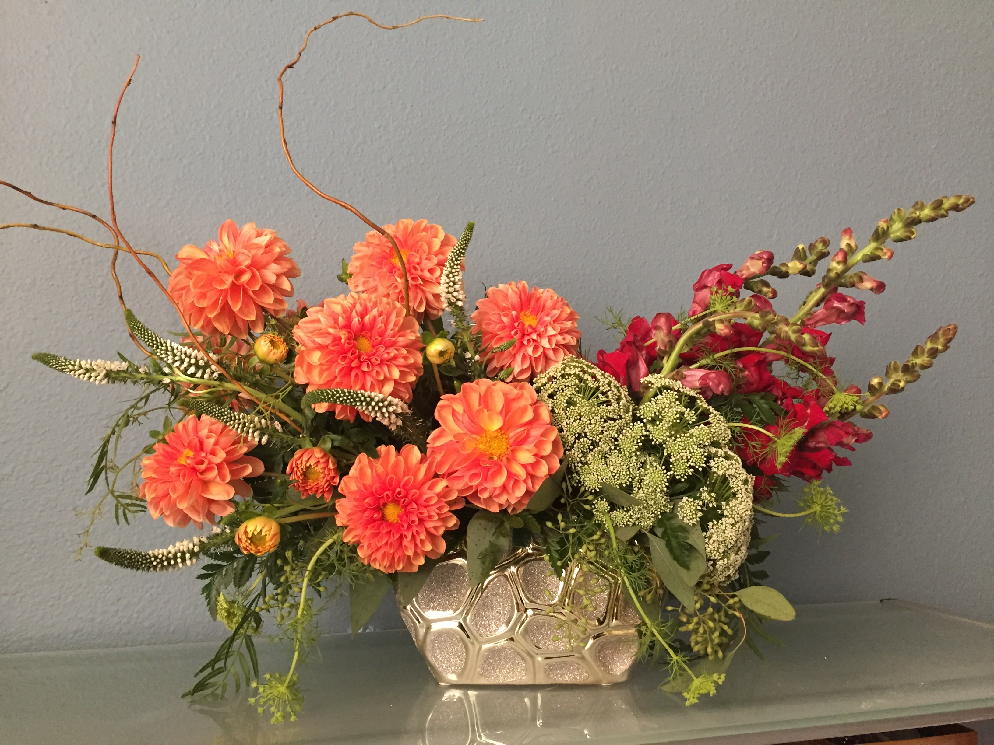 Citrus Kissed Bouquet - As warm and inviting as a day at the beach or summer sunrise, this invigorating arrangement of mouthwatering orange flowers is a gorgeous expression of your love or friendship.  •Orange dahlia, burgundy snapdragon, white veronica bulk flowers, queen anne's lace are gathered with fresh green bupleurum and pittosporum in a  gold vase. •Orientation: All-Around 