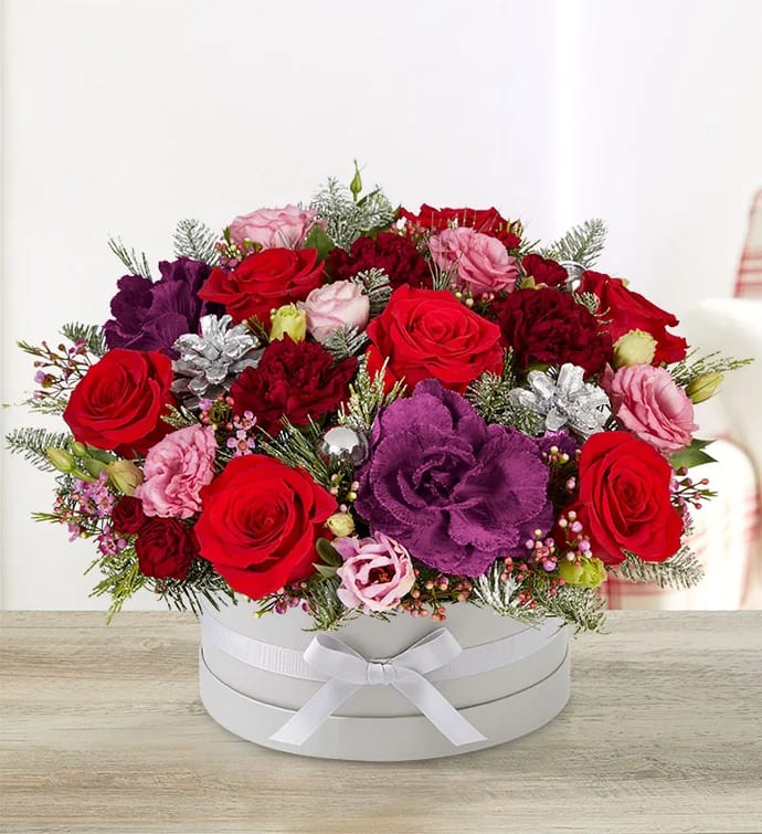 Winter Delight - Round arrangement with red roses, pink carnations, burgundy carnations &amp; mini carnations, purple carnations and waxflower. Accented with silver frosted pinecone picks, silver ball ornaments and assorted Christmas greenery.
