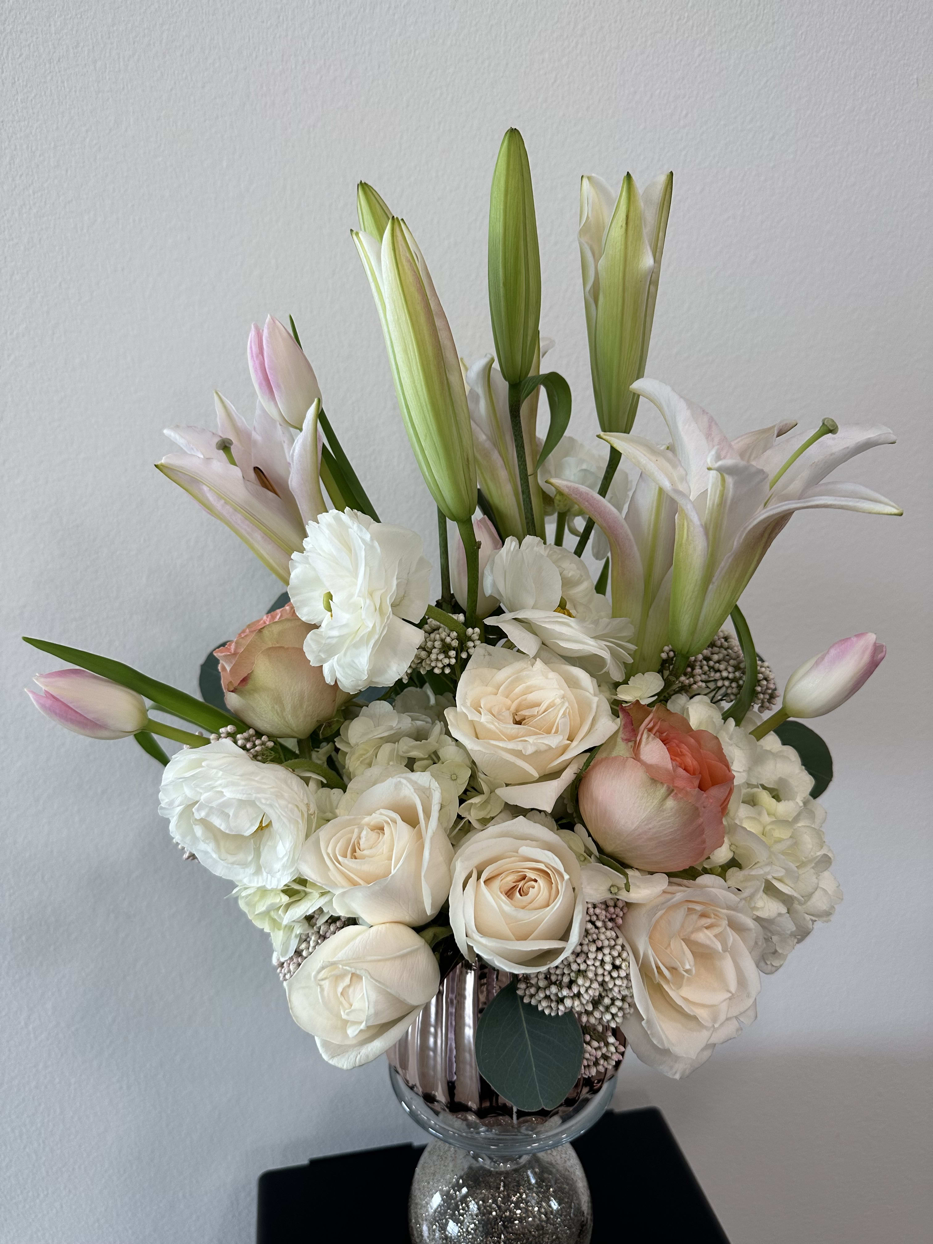 eternal pink - A combination of pink tulips mixed with pink lilies, white ranunculus, soft pastel roses, and apricot color roses, on a bed of white hydrangeas