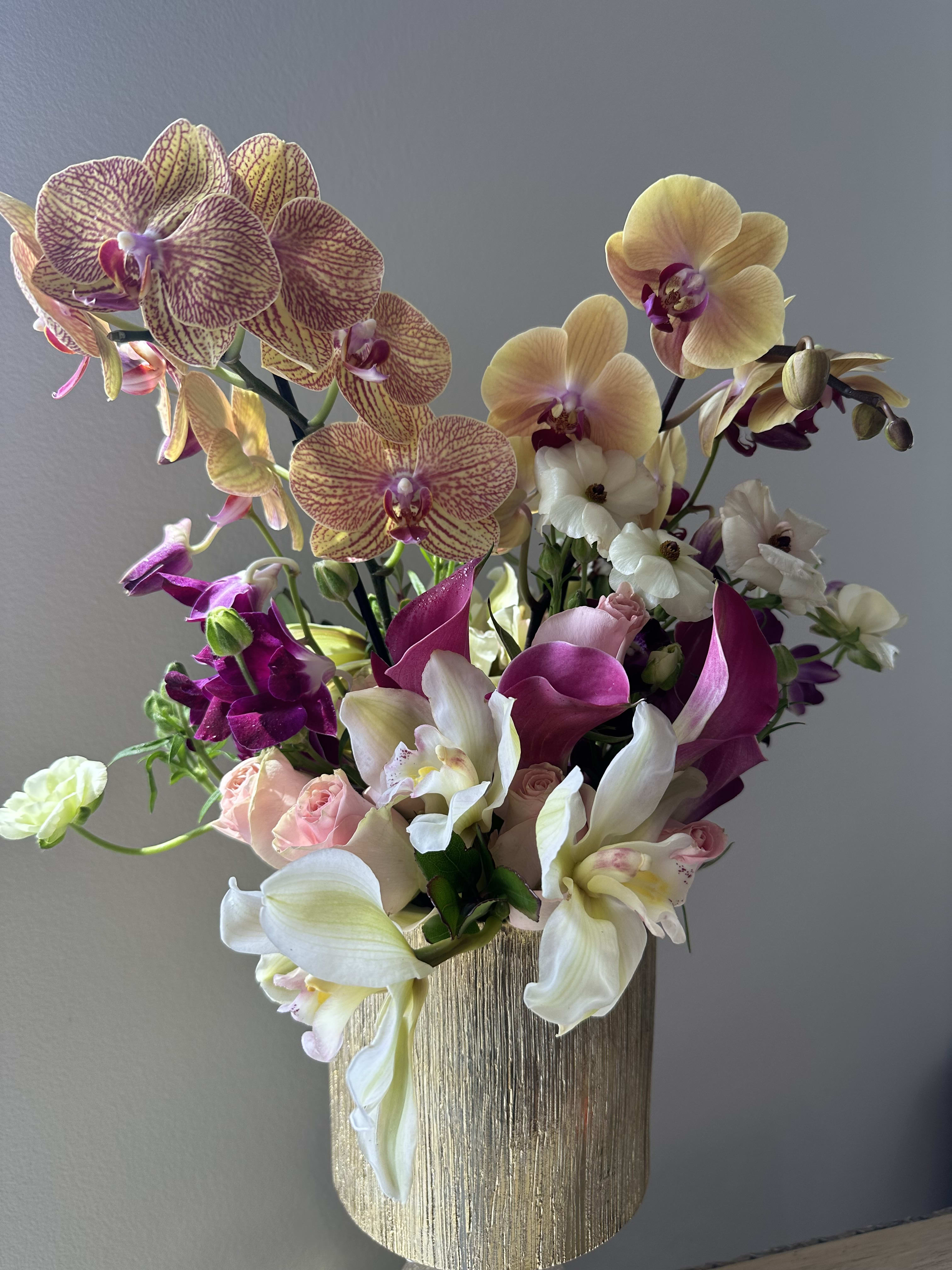 splash of pink island - A gorgeous combination of Phalaenopsis Orchids mixed with Cymbidium orchids, purple  mini Cala lilies, light pink roses, in a beautiful gold ceramic container
