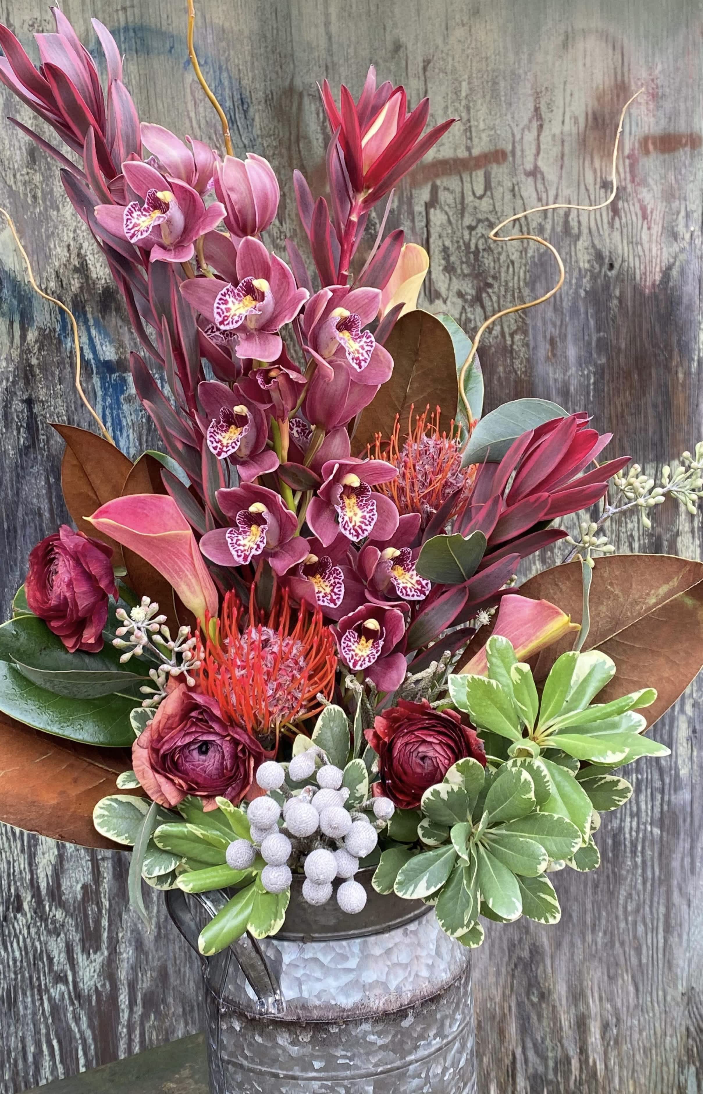 Rustic reds - Tall vase arrangement with cala lilies, orchids, ranunculus, and protea. 