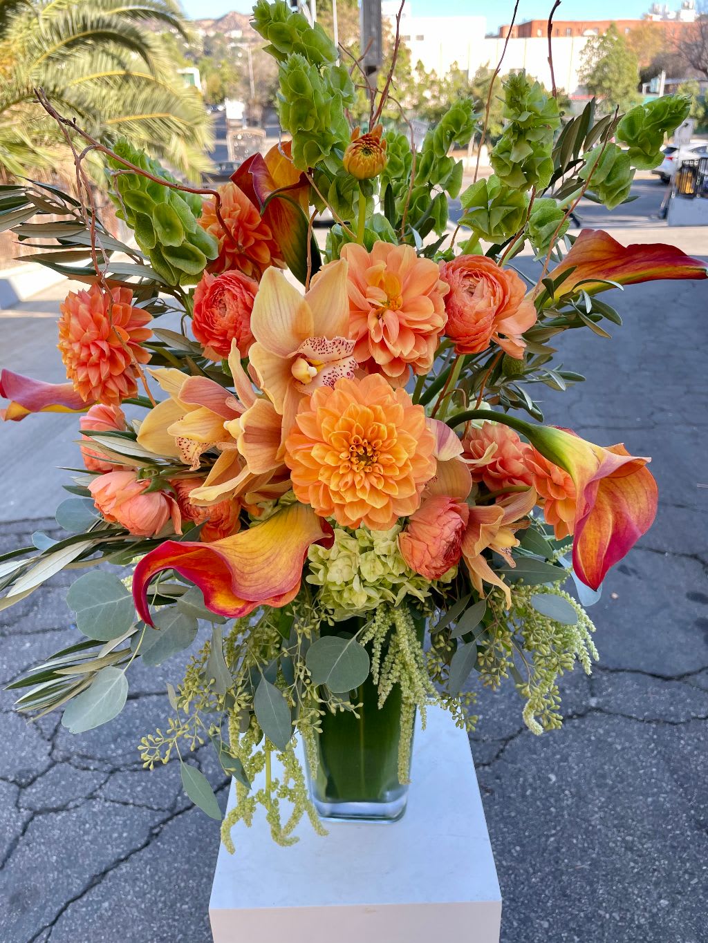California  Sunset - Welcoming the fall with rich tones of Orange Calla lilies, Orchids, Proteas Burgundy hanging Amaranthus and more.  This bouquet is the perfect way to celebrate the arrival of fall. The rich tones of orange, burgundy, and purple are reminiscent of the changing leaves and the cozy feeling of the season.  Orange calla lilies represent joy, happiness, and new beginnings. They are also associated with the fall season, as they are often in bloom during this time of year.  Orchids are a symbol of elegance, beauty, and luxury. They come in a variety of colors, including orange, burgundy, and purple.  Proteas are a type of flower that is native to South Africa. They are known for their unique and exotic appearance. Proteas represent courage, strength, and transformation.  Burgundy hanging amaranthus is a type of flower that is known for its long, hanging stems. It is often used in dried flower arrangements. Burgundy hanging amaranthus represents love, passion, and immortality.  Together, these flowers create a bouquet that is both beautiful and meaningful. It is the perfect way to celebrate the fall season and to show someone how much you care about them.  Here are some ideas for how to present this bouquet to your loved one:  Give it to them as a surprise gift. Leave it on their pillow when they go to bed. Bring it to them at work. Place it in a vase in their favorite room. Use it as a centerpiece for a fall gathering. No matter how you choose to present it, this bouquet is sure to be a hit.  Visit Dave's Flowers online or in-store in Los Angeles to discover this breathtaking fall bouquet and explore our wide selection of seasonal arrangements. We offer convenient flower delivery in Los Angeles to ensure your floral masterpiece arrives fresh and ready to bring autumn's beauty into your life.