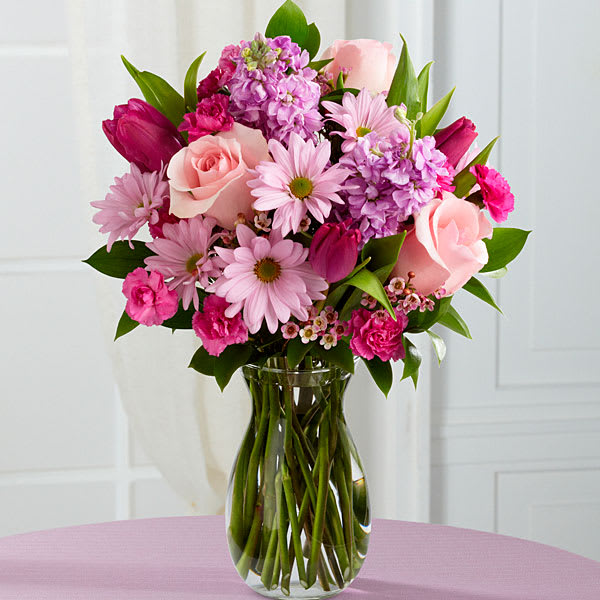 Sweet Delight Bouquet - Pink roses, purple tulips, lavender stock, lavender traditional daisies, fuchsia mini carnations, lavender waxflower and lush greens are brought together in a clear glass vase.